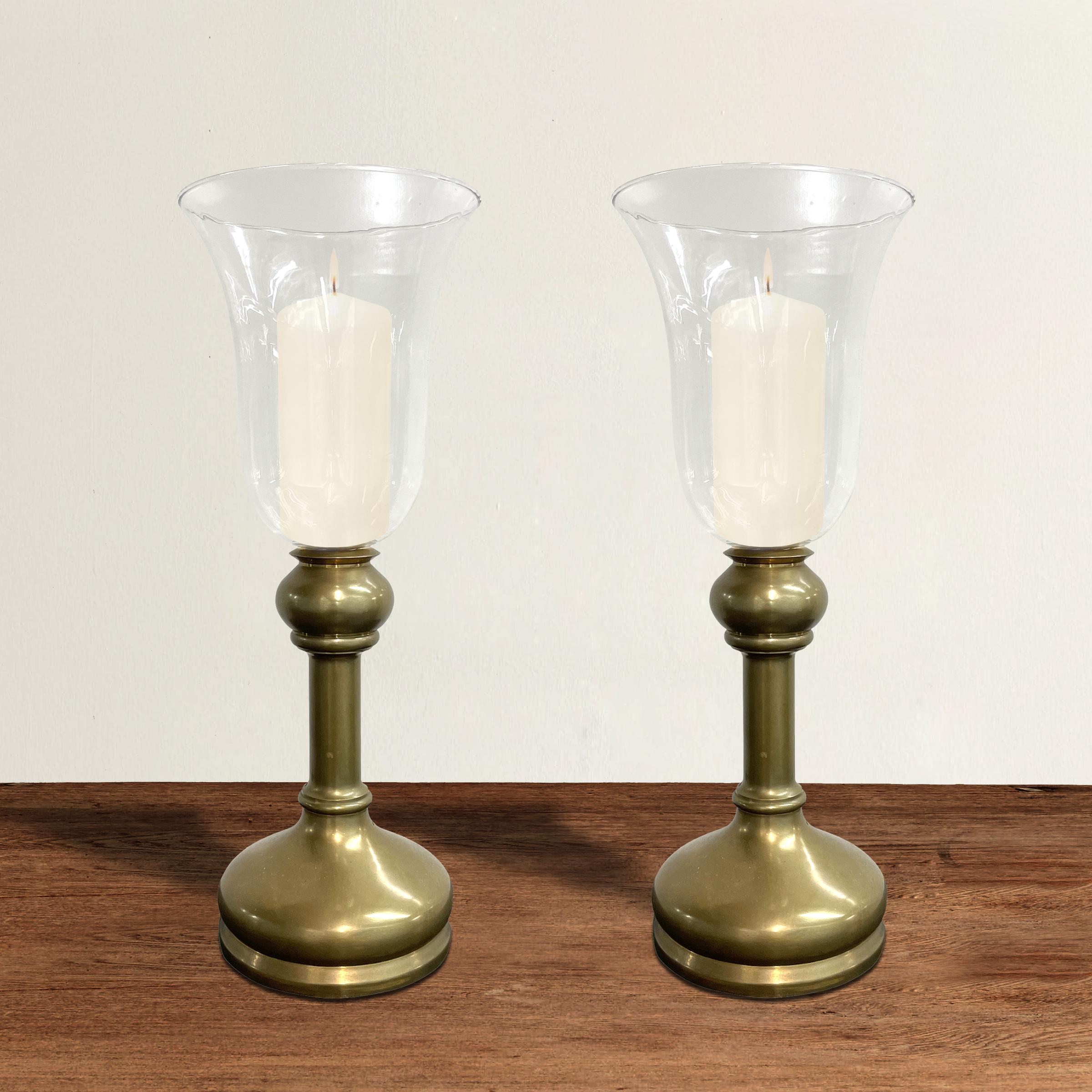 A pair of vintage 20th century heavy brass candlesticks with bell-shape glass hurricanes.