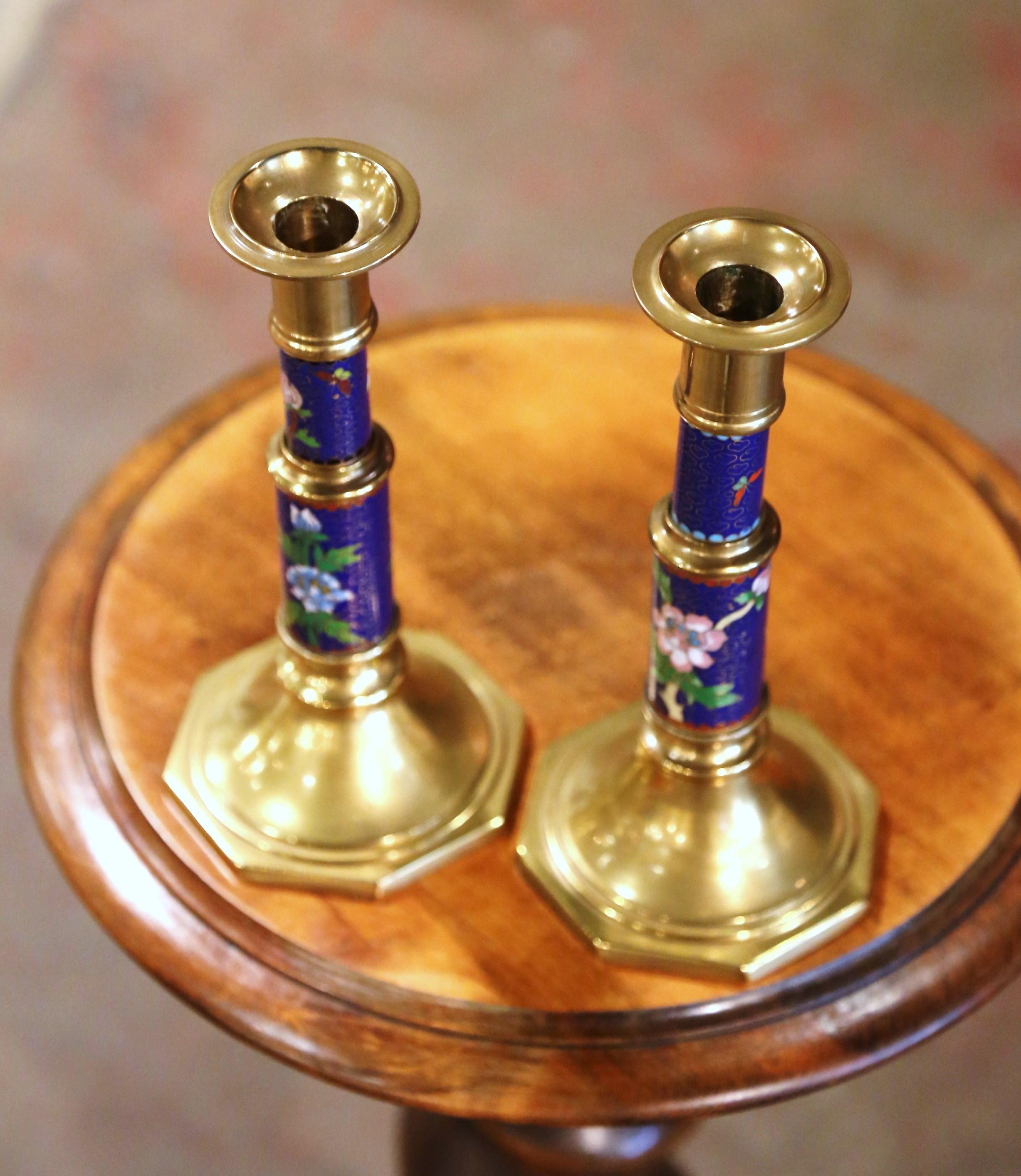 Add timeless elegance to your space with this colorful pair of antique patinated brass candlestick holders. Crafted in China, circa 1970, each candlestick features intricate cloisonné décor with vibrant flower, leaf and bird motifs. Perfect for a