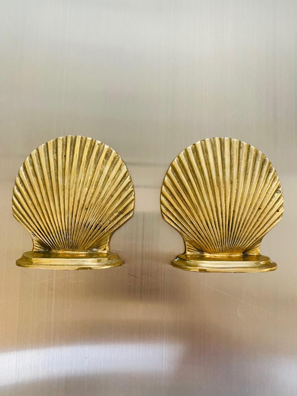 Pair of vintage brass sea shell bookends, circa 1970s. This beautiful pair of Hollywood Regency style sea shell bookends will brighten any space with their joyful gilt. This pair will enhance your mid-century, Hollywood Regency or eclectic decor