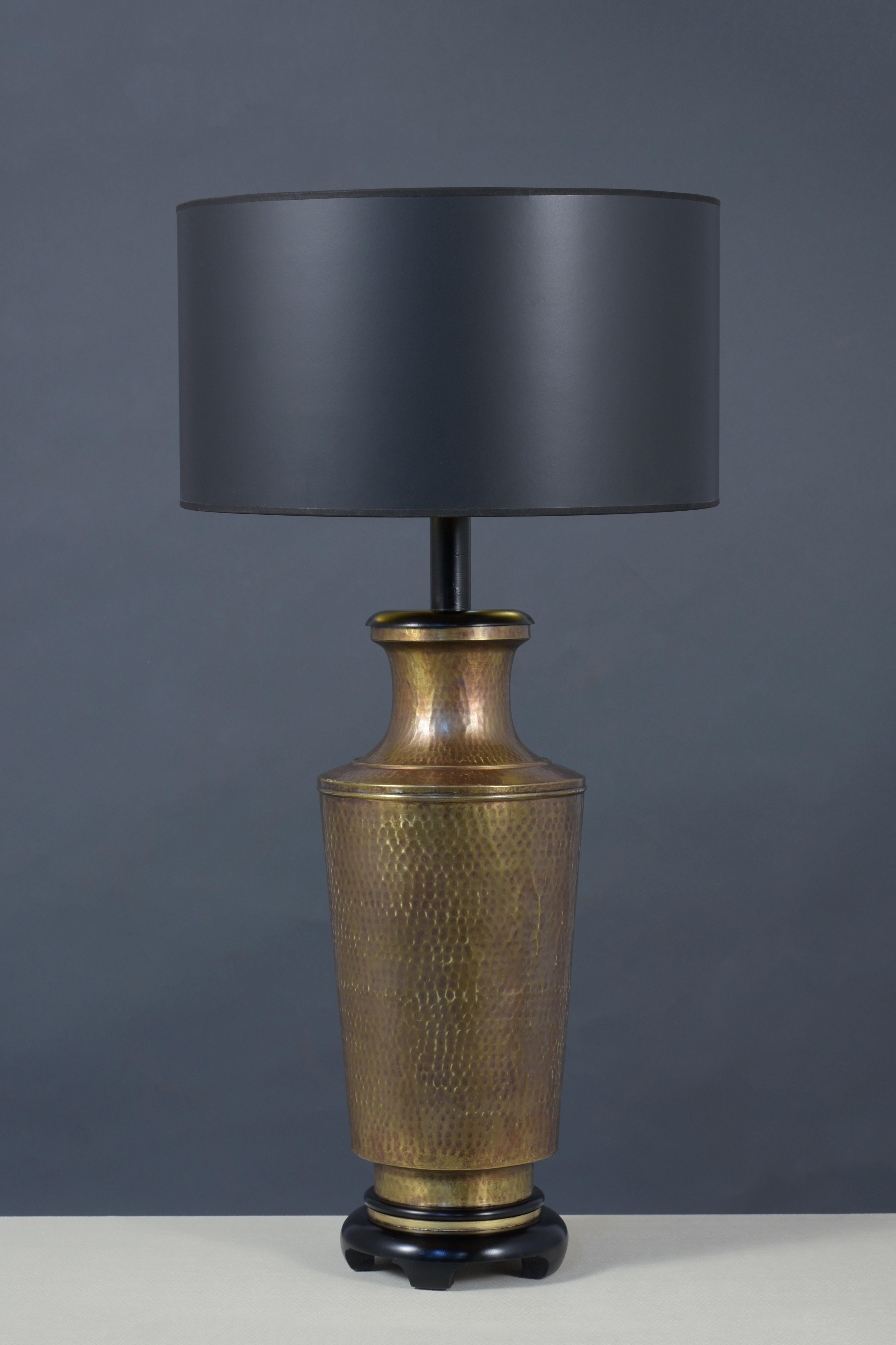 A pair of vintage table lamps handcrafted out of brass these pair of lamps have been fully restored and are wired for U.S standards and features new black and gold color interior shades a large eye-catching hammered design vase sitting on a carved