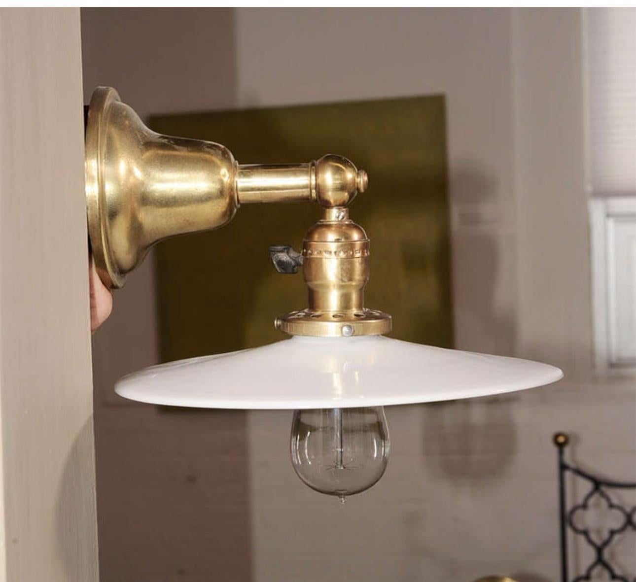 Pair of vintage brass wall lights / sconces with antique white milk glass disk shades. USA, circa 1910.

Dimensions:
4.5 inch wall plate diameter (part that mounts to wall) 
9 inch depth overall/projection from wall (including shade)
8 inch width