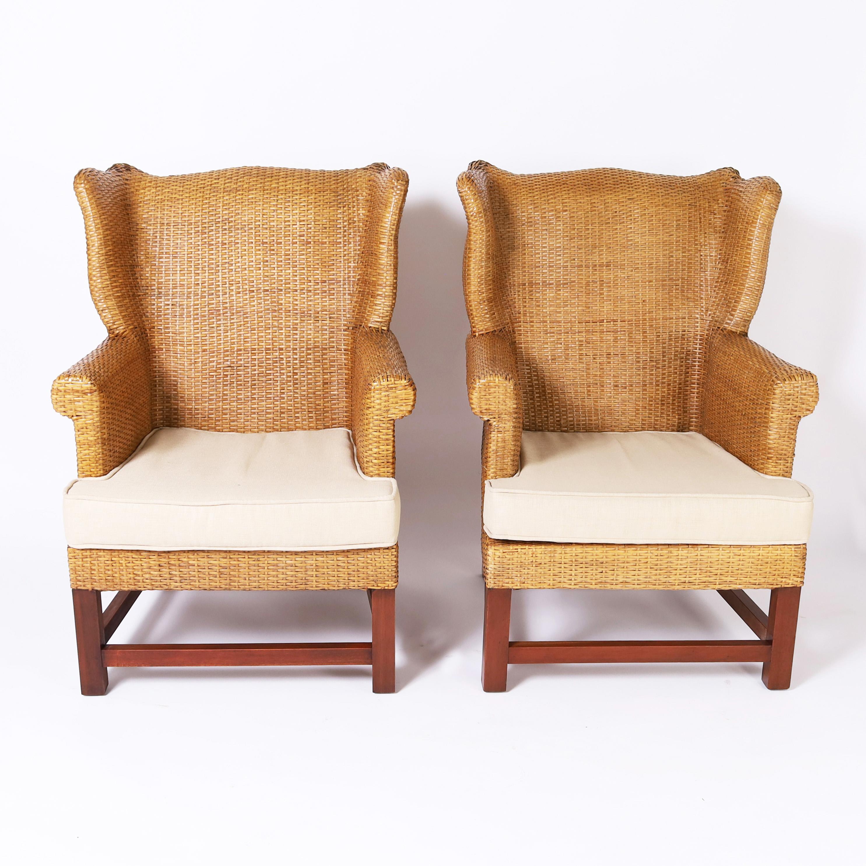 Impressive pair of vintage British colonial style wingback armchairs upholstered in grass cloth or woven reed in classic comfortable form with a modern tropical twist, cotton cushions and mahogany Chippendale style stretchers and legs. 