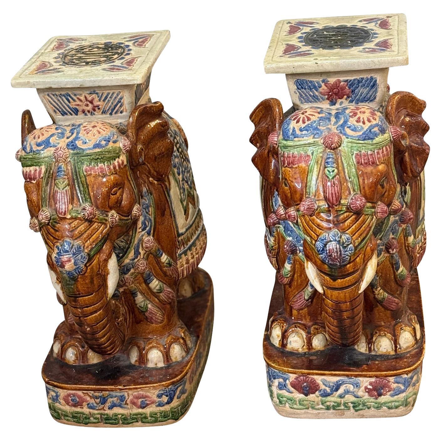 Ein Paar aus Braun und Grün und  blau asiatischen Elefanten Garten Hocker mit Gold Farbe und Creme Farbe Sättel und trimmen. Jeder Hocker stellt einen Elefanten mit erhobenem Rüssel dar. Diese bezaubernden Hocker eignen sich perfekt als Beistell-