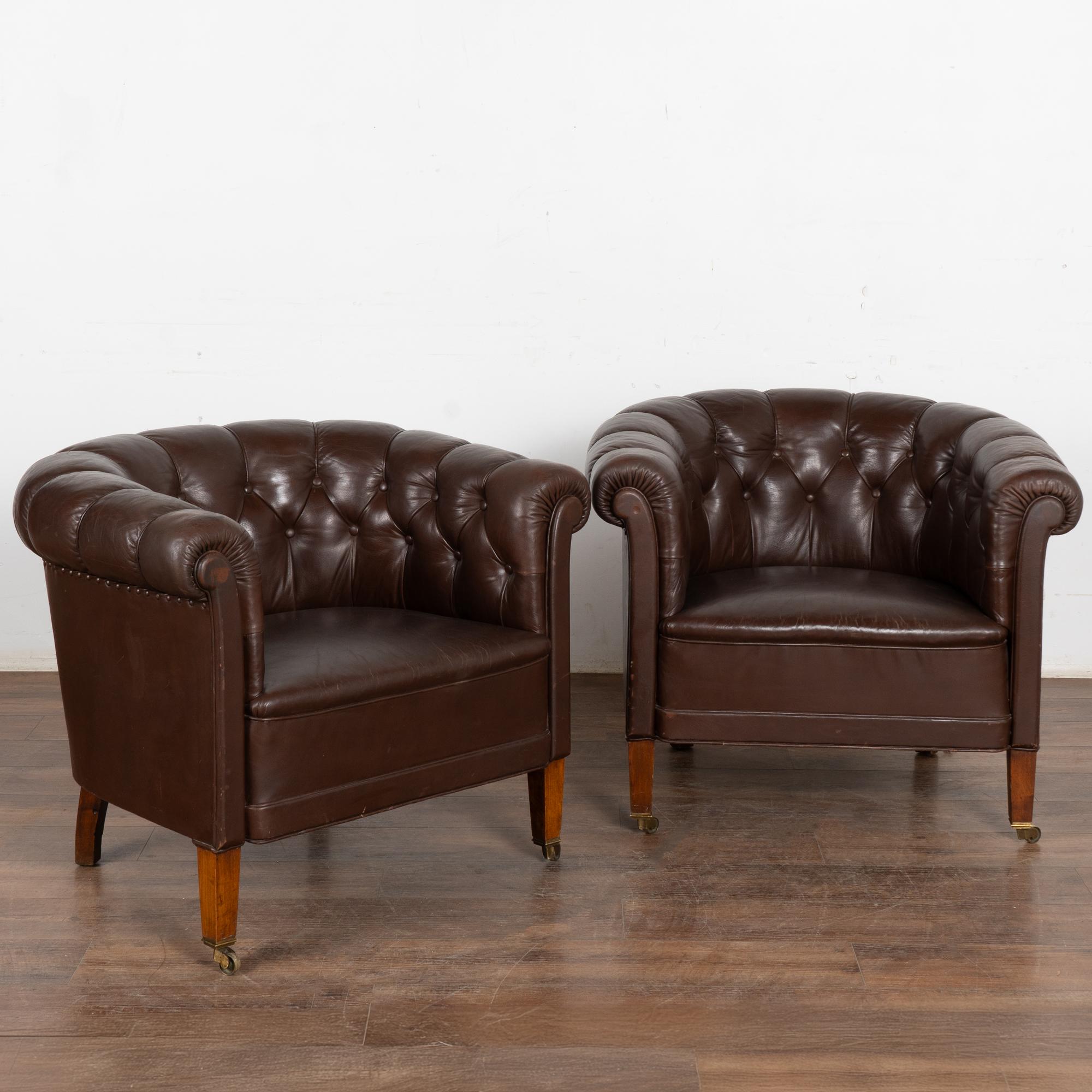 This pair of vintage leather club chairs are welcoming with barrel shaped arms and tufted backs with self covered buttons and piping; castor feet.
This pair shows signs of typical age and wear to the dark brown leather including scratches, stains,
