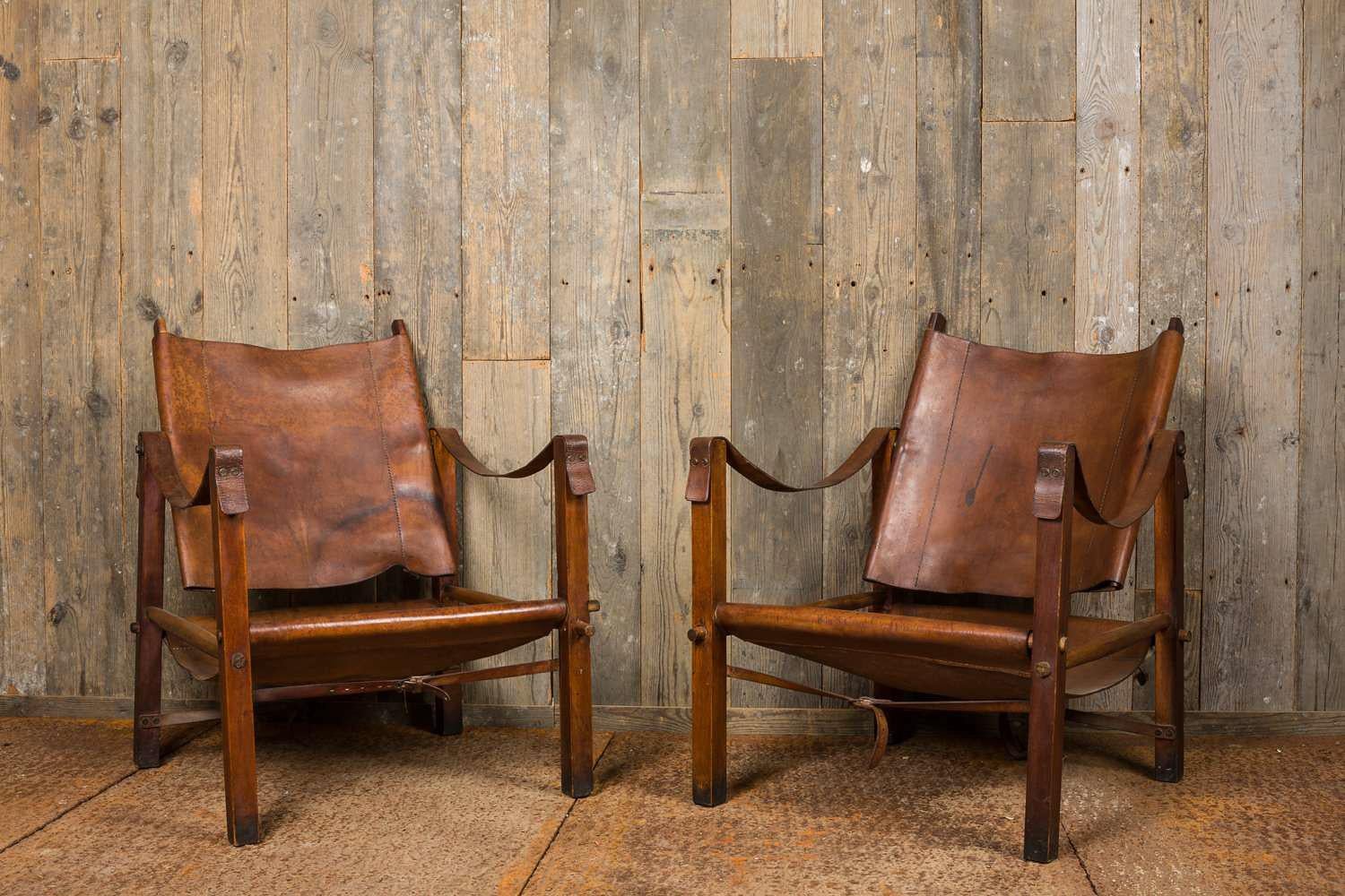 Pair of Scandinavian leather safari chairs in the manner of Arne Norell or Kaare Klint. Vintage armchairs with walnut wooden legs and pitch pine horizontals. The seating, the swing backrests, the armrests and leather belt straps are of brown /