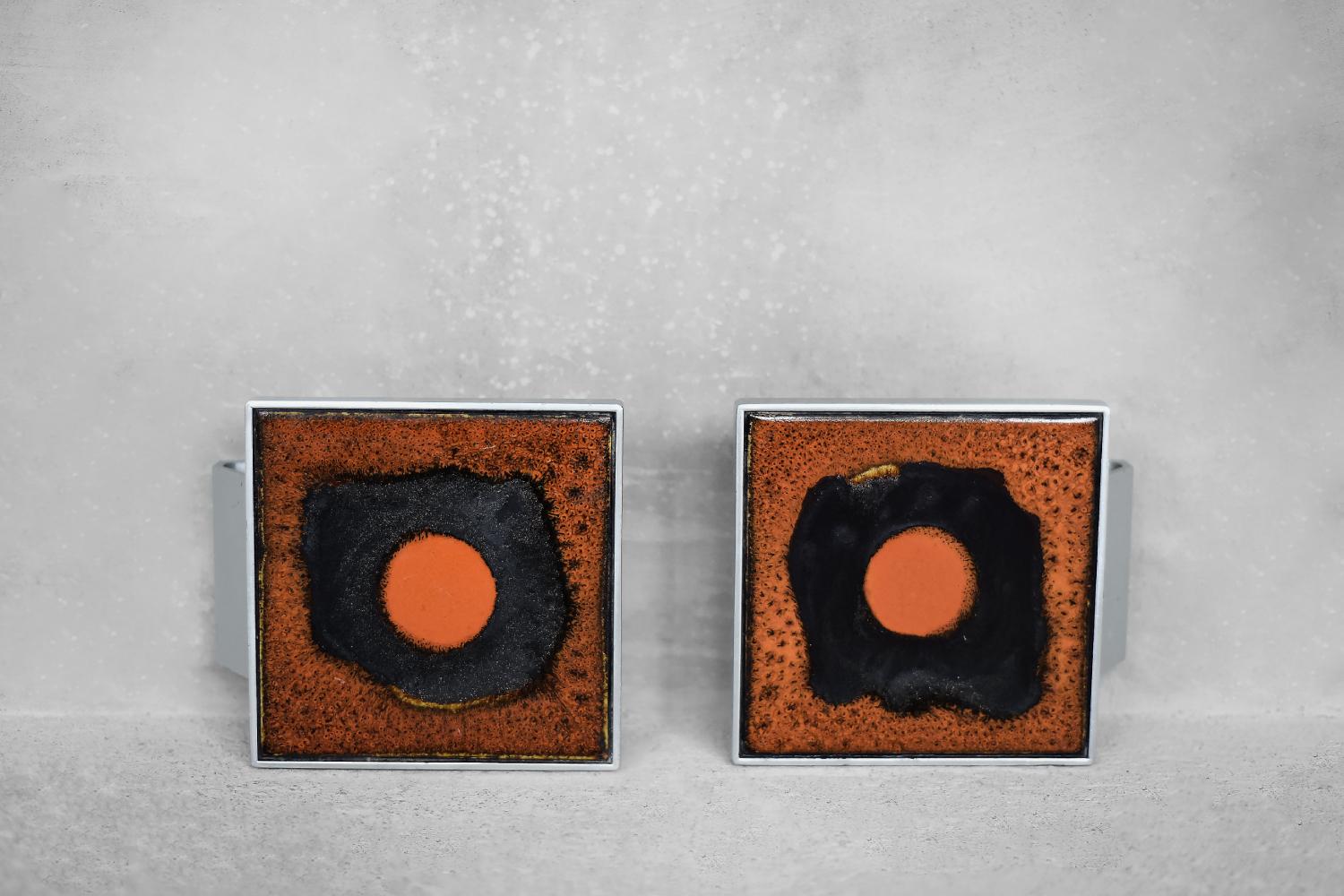 This pair of original door handles was designed and made by the Belgian artist Juliette Belarti during the 1960s. The geometric frame is made of aluminum and the center is filled with an orange and black glazed ceramic board. The combination of