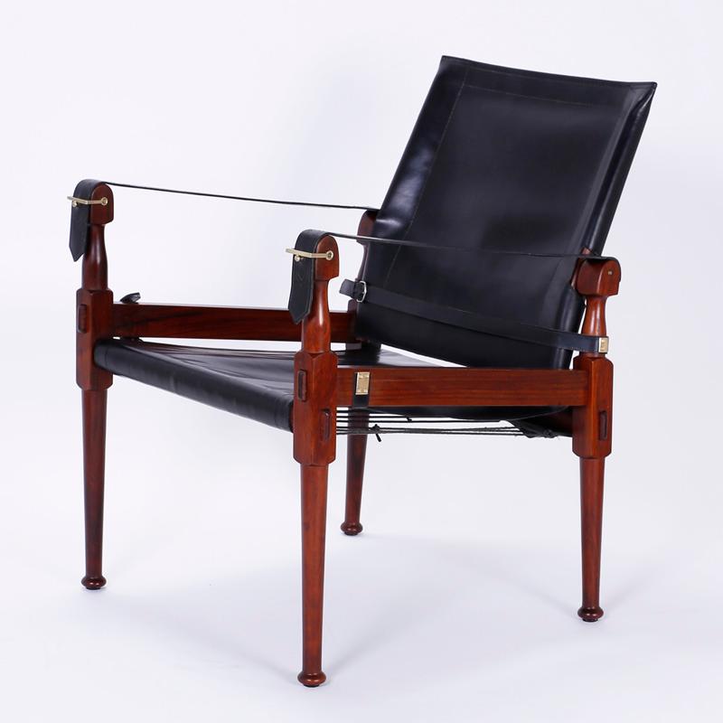 Pair of vintage safari chairs with a confident debonaire stance constructed with well appointed mahogany, turned and mortised. Having black leather seats and backs. The arms are distinctive leather straps held by chic brass buckles. Attributed to M