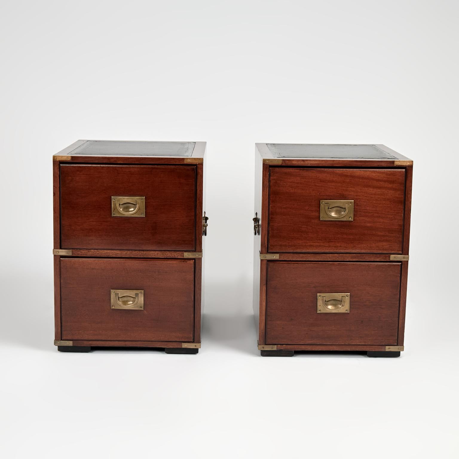 Handsome pair of vintage British Colonial style stands crafted in mahogany with two drawers, having tooled leather tops, campaign brass hardware and block feet. Signed Burton Reproductions Limited England in a Drawer. 