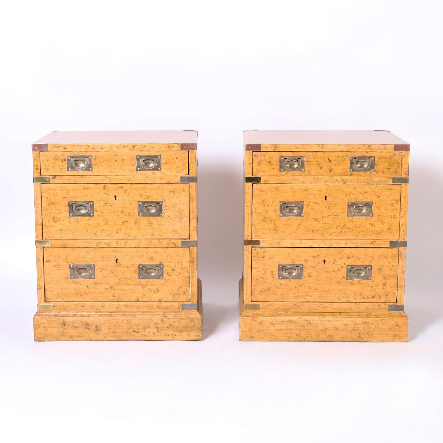 Standout pair of mid century three drawer stands or chests having a faux ostrich finish, brass campaign style hardware and block feet. Signed Trouvailles in a drawer.