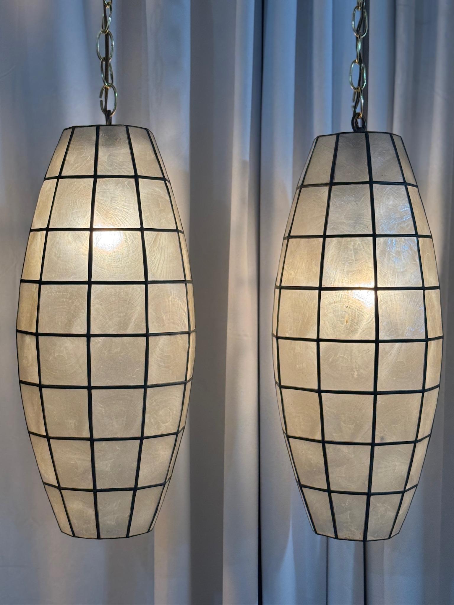 Illuminate your space with this exquisite pair of vintage Capiz shell pendant lights, exuding a warm and inviting glow. These beautifully handcrafted fixtures feature an elongated oval form, allowing light to be softly diffused through the genuine