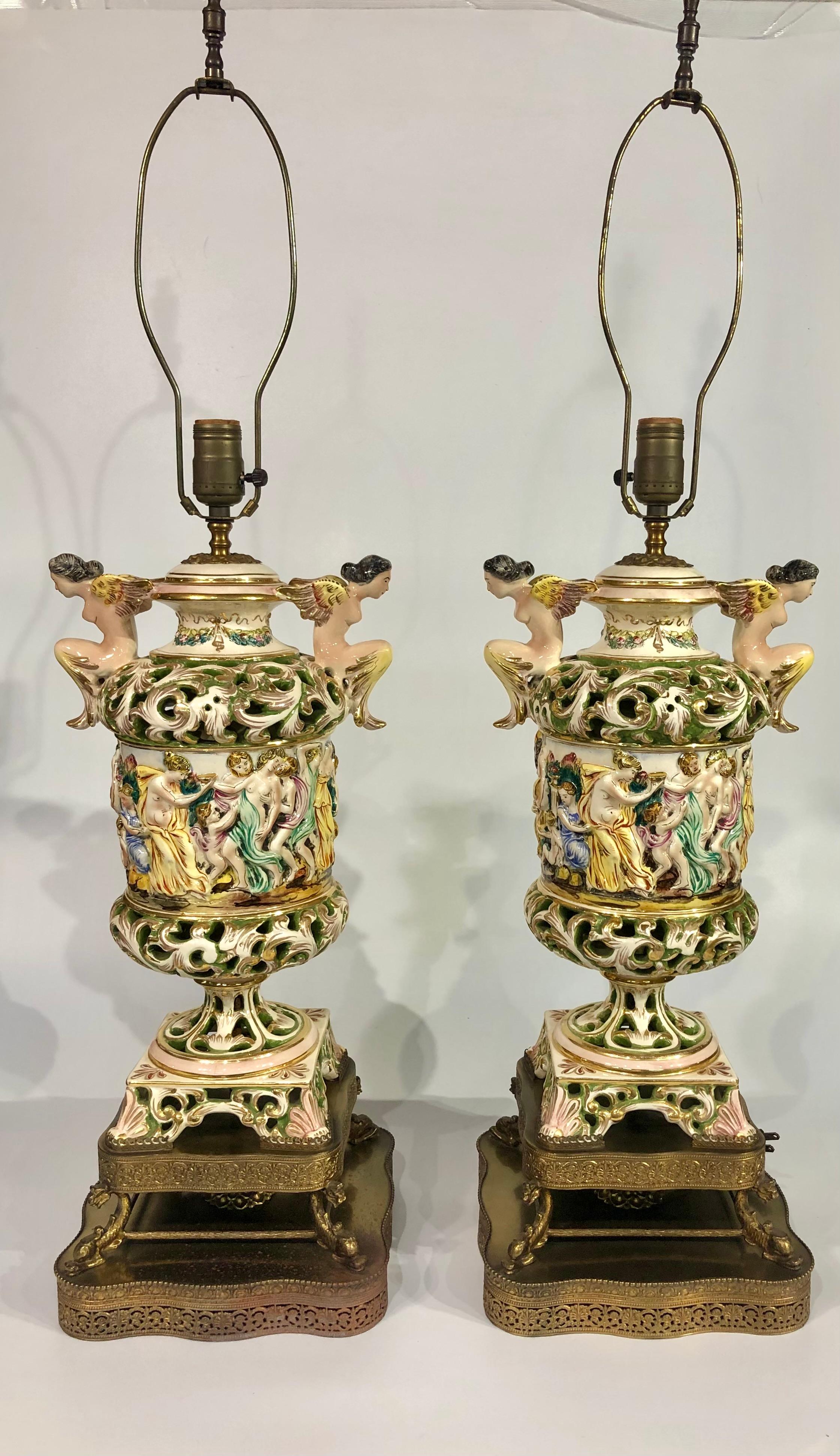 Esta impresionante pareja de lámparas de porcelana figurativa de Capodimonte de principios del siglo XX es una auténtica obra maestra del arte italiano. Estas lámparas de mesa de cerámica, elaboradamente pintadas, representan vibrantes escenas de
