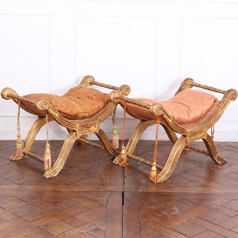 A pair of vintage carved and gilt ‘X’ frame stools with reeded frames and scrolled ends.

