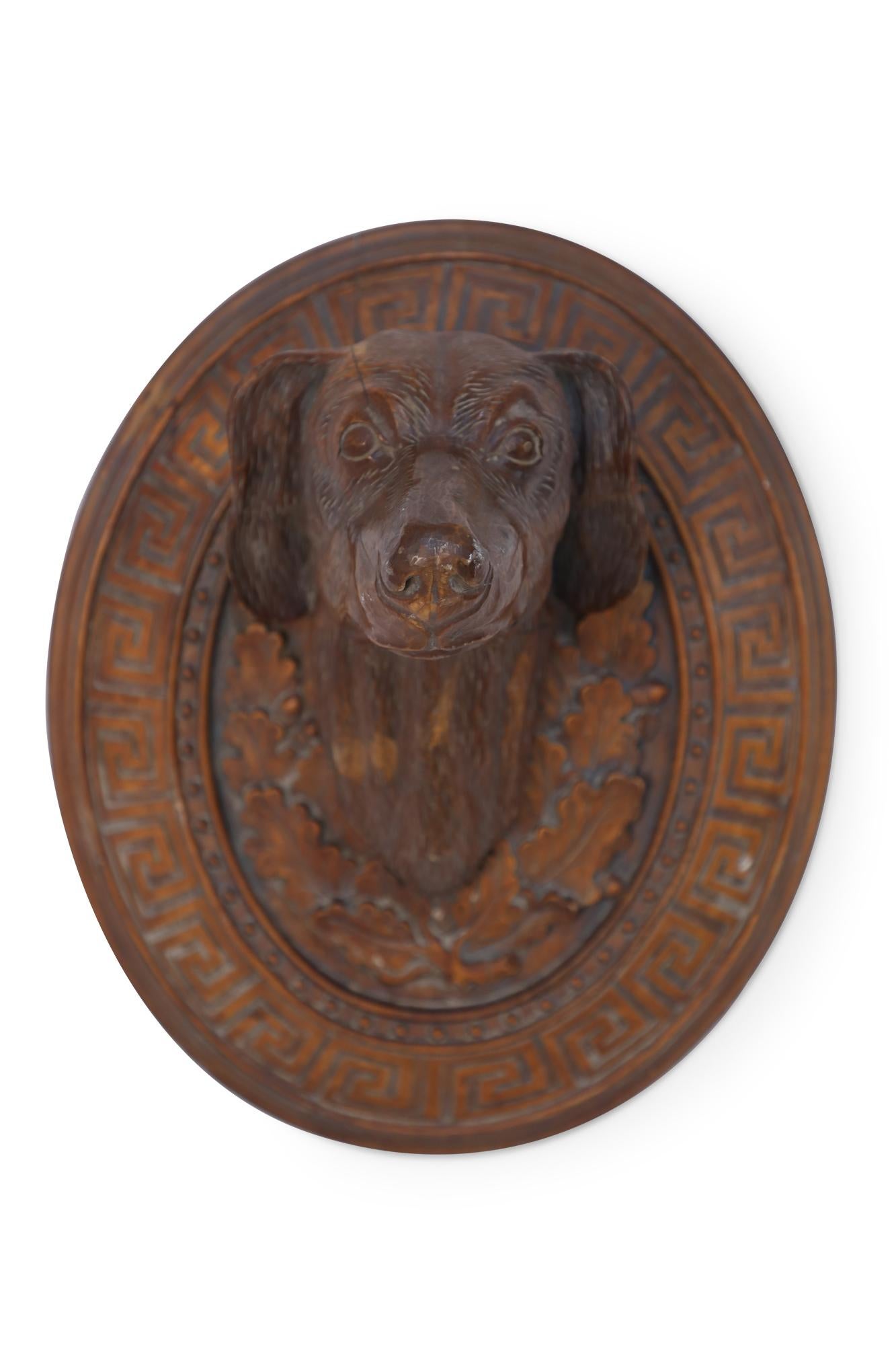 Pair of similar vintage carved wooden wall plaques featuring centered dog heads surrounded by acanthus leaves and a Greek key border.