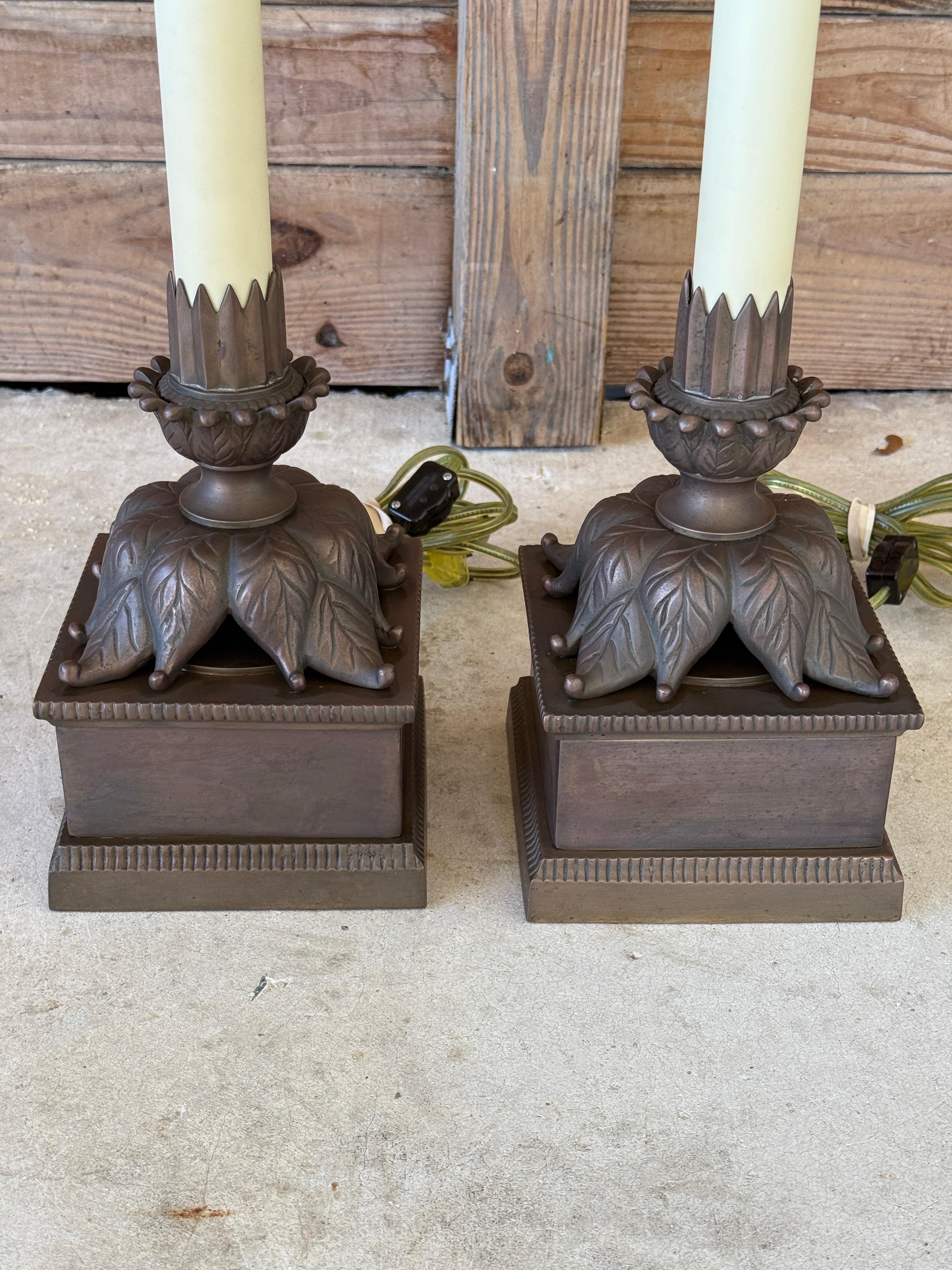 A striking pair of vintage Chapman table lamps, crafted with bronze patinated metal bases featuring stylized acanthus leaf and fluted candle designs. Each lamp retains its original harp and flame finial, showcasing Chapman’s signature quality and
