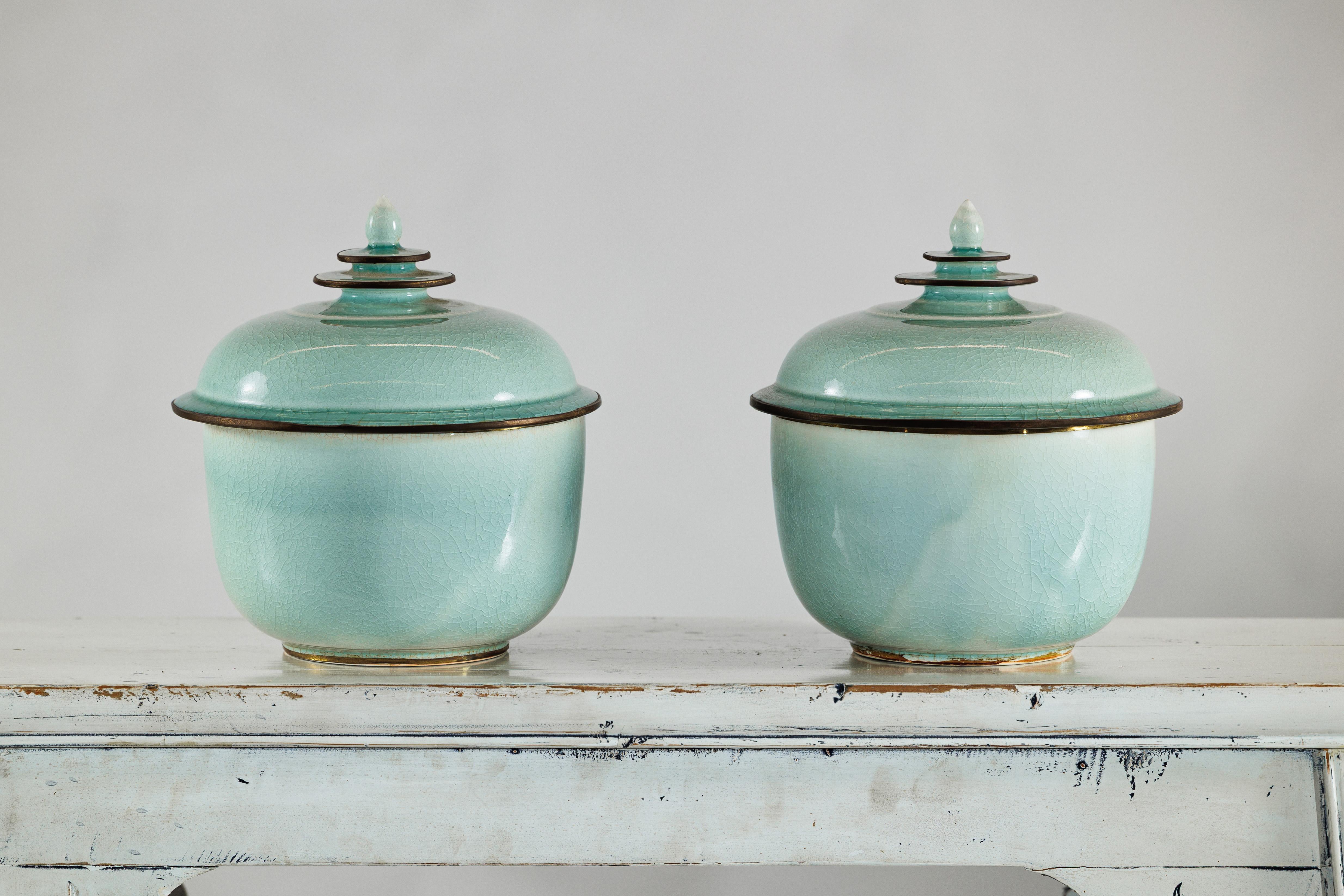 Una graziosa coppia di vasi in ceramica cinese d'epoca in smalto celadon, ciascuno con un coperchio a cupola coronato da un terminale a gradini. I corpi morbidamente arrotondati sono caratterizzati da un'ampia bocca  (con un diametro di 8,5