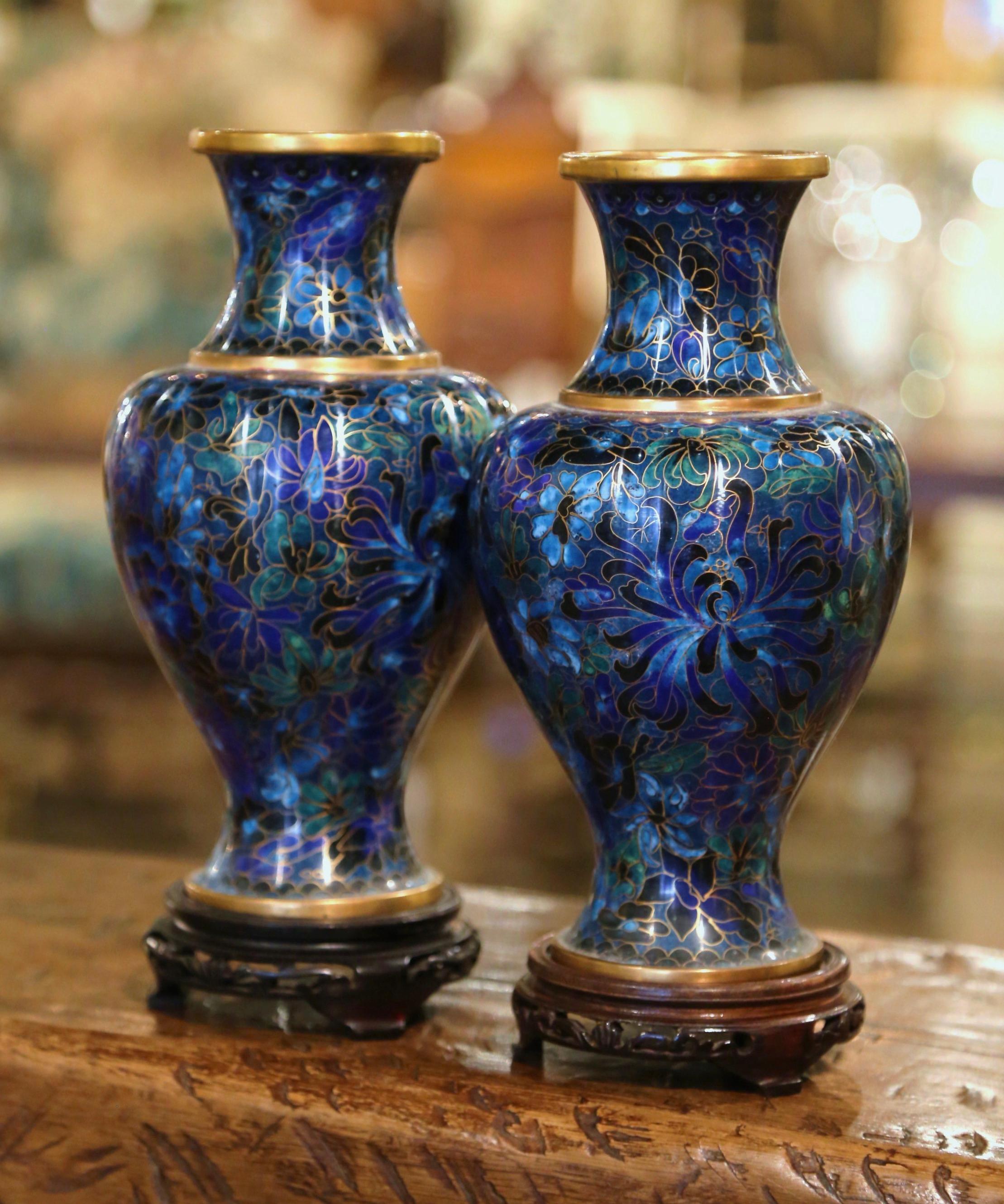 Decorate a mantel with this colorful pair of baluster vases; created in China circa 1980, each vase sits on a carved ebonized wood stand and features floral motifs in the cloisonné technique (decorative work in which enamel, glass, or gemstones are