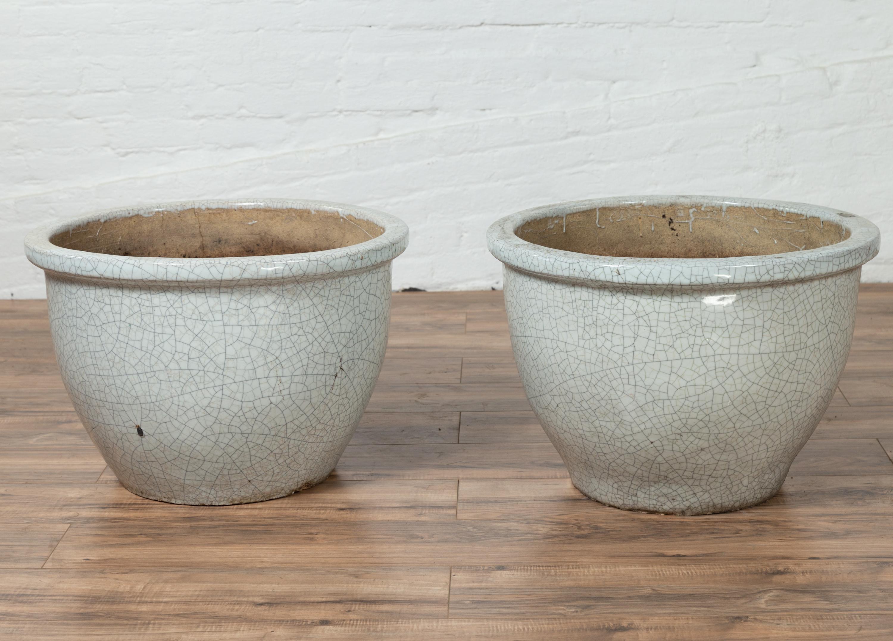 A vintage pair of Chinese large cracked celadon planters from the mid-20th century. Born in China during the midcentury period, each of this pair of large planters features a circular tapering body, accented by a stylish cracked celadon finish.