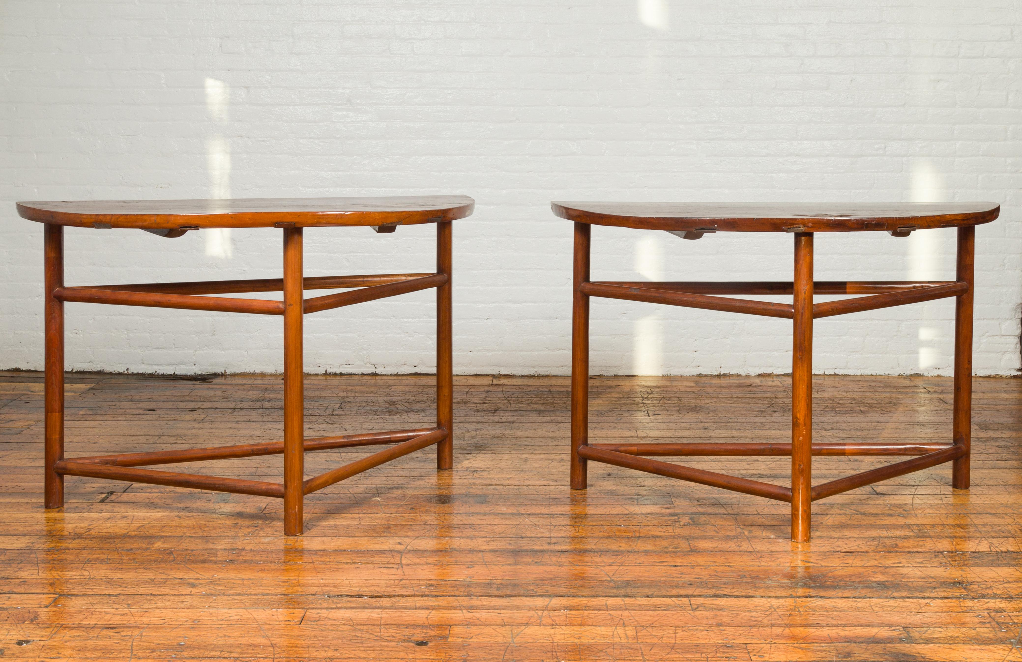 A vintage pair of Chinese demilune console tables from the mid-20th century, with semi-circular top and triangular stretchers. Born in China during the midcentury period, each of this pair of demilune tables features a semi-circular top sitting
