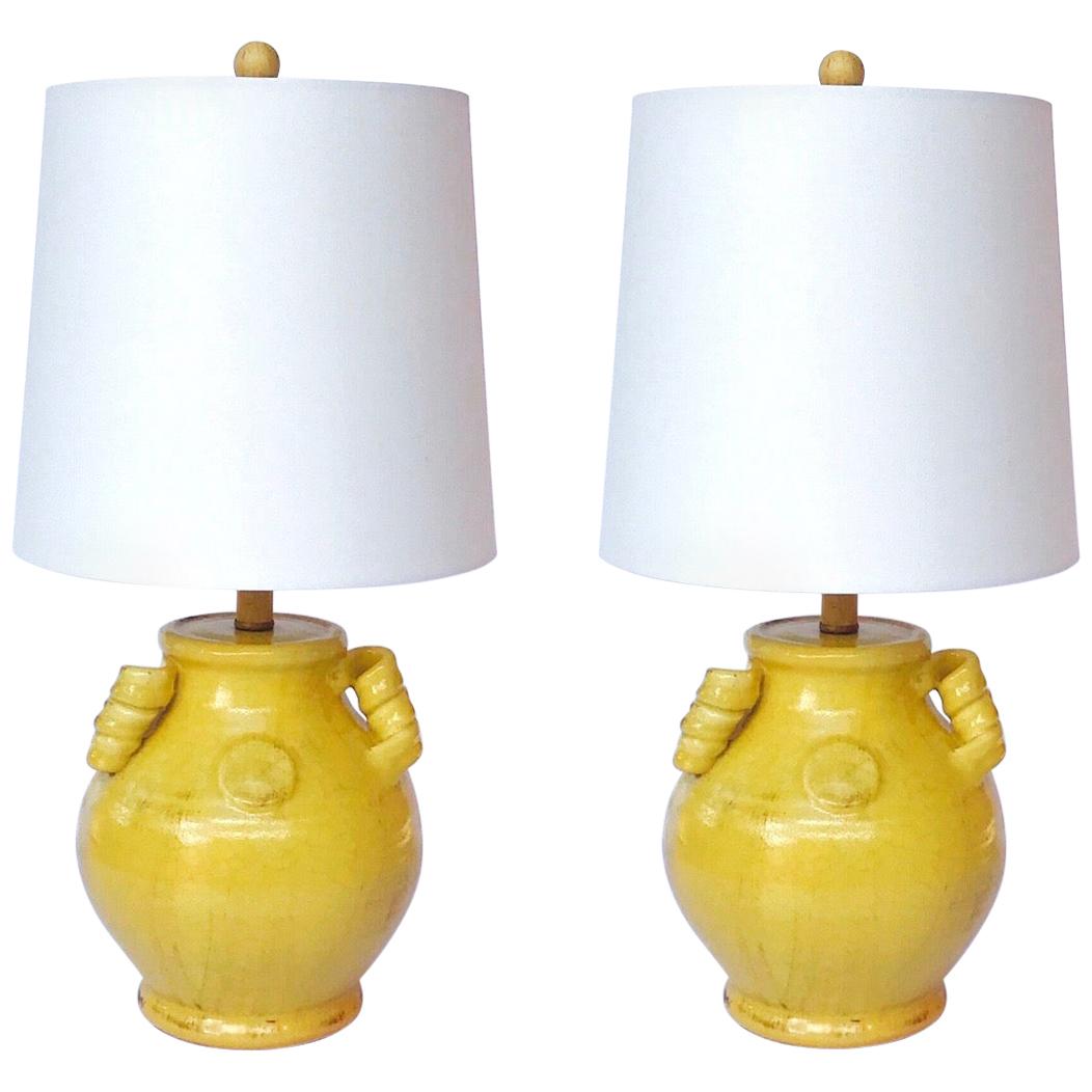 Pair of Chinoiserie Hollywood Regency ceramic urn lamps. Handcrafted in a beautiful yellow crackle glaze finish with hand painted antiqued patina effect. Lamp features three handles with stylized spirals. Shown with new custom drum shades in white.