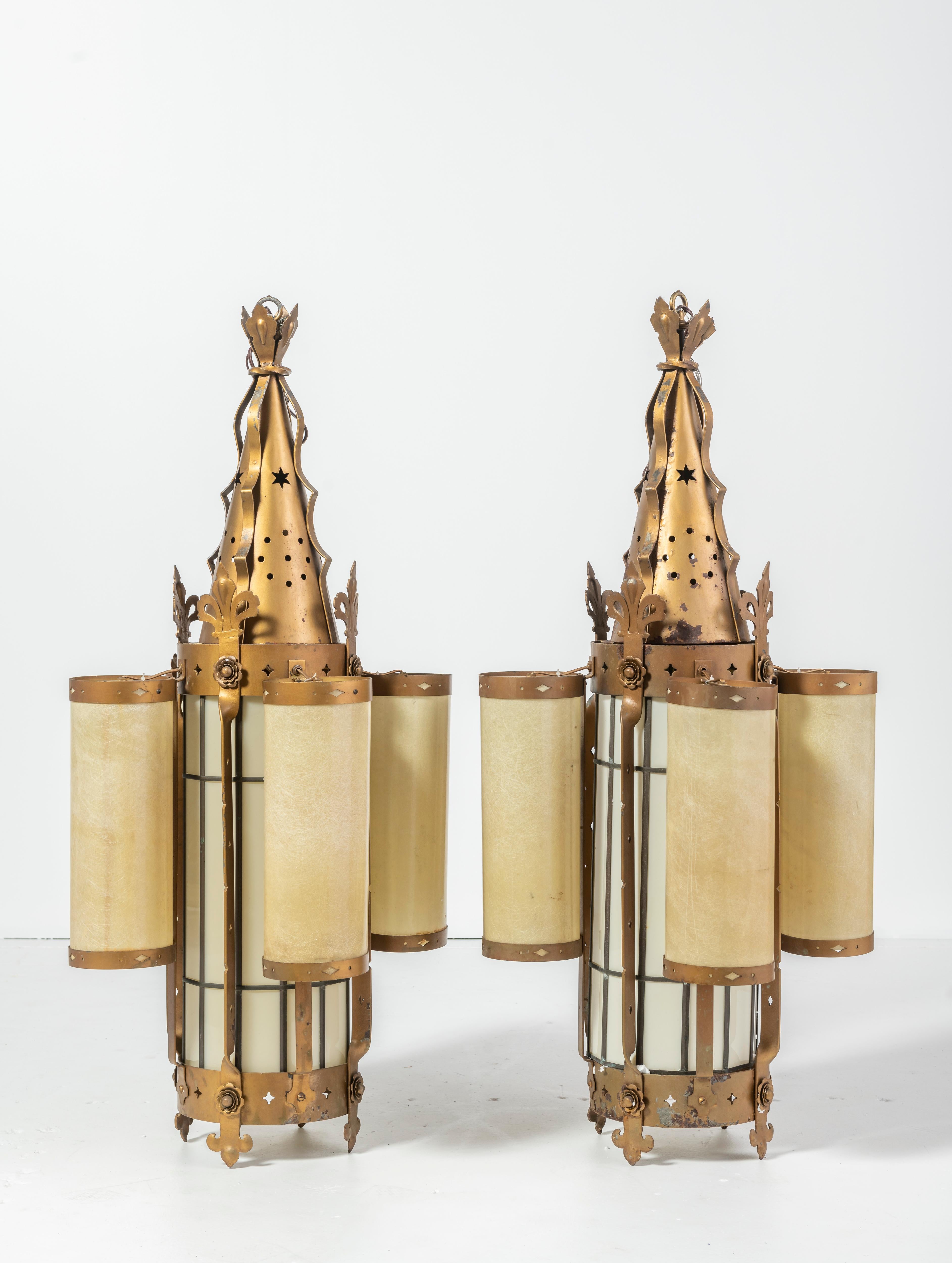 Vintage pair of ornate pendants in brass, ivory and amber fiberglass, which casts a lovely, soft light. Rare design with 4 light columns circling 1 center light. Brass patina is chipped in a few places though in overall good condition given the age.