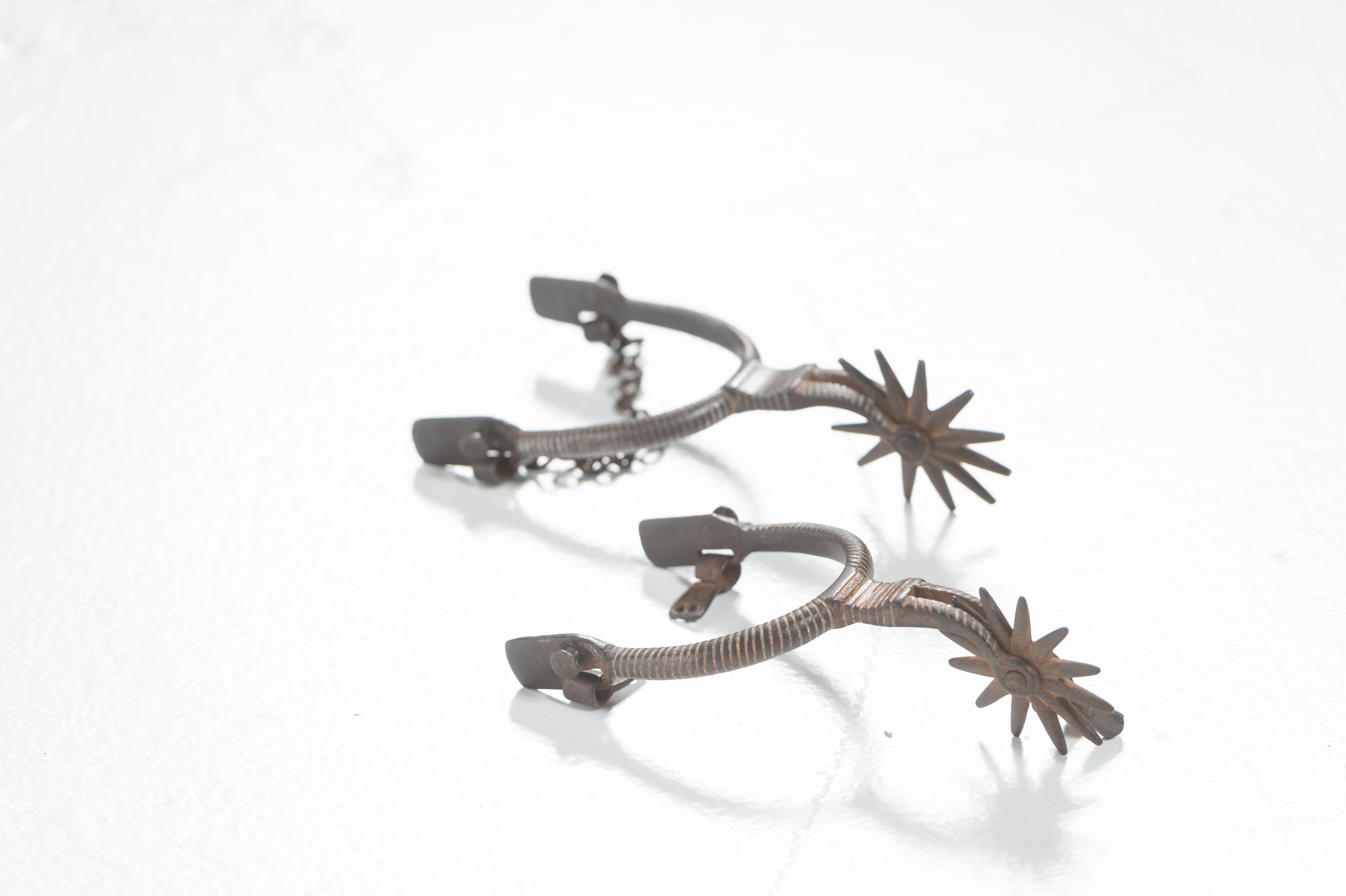 Pair of vintage cowboy spurs, thought to be of Mexican origin. Made in early 20th Century, the spurs are of iron inlaid with silver (content unknown) and have twelve-point star rowels. Great addition to any collection, cowboy or otherwise.