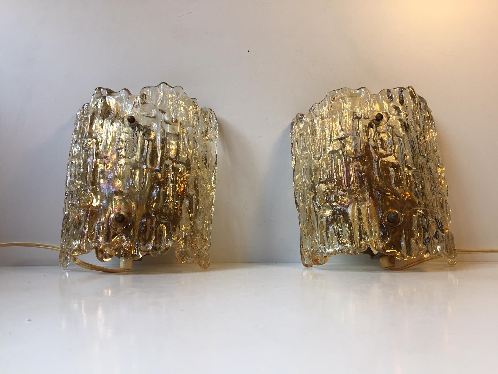 This pair of Mid-Century Modern sconces by Carl Fagerlund was manufactured by Orrefors in the 1950s-1960s. The textured crystal shading creates a cosy and soft lighting. The set features brass mounts and screws and is in working condition.