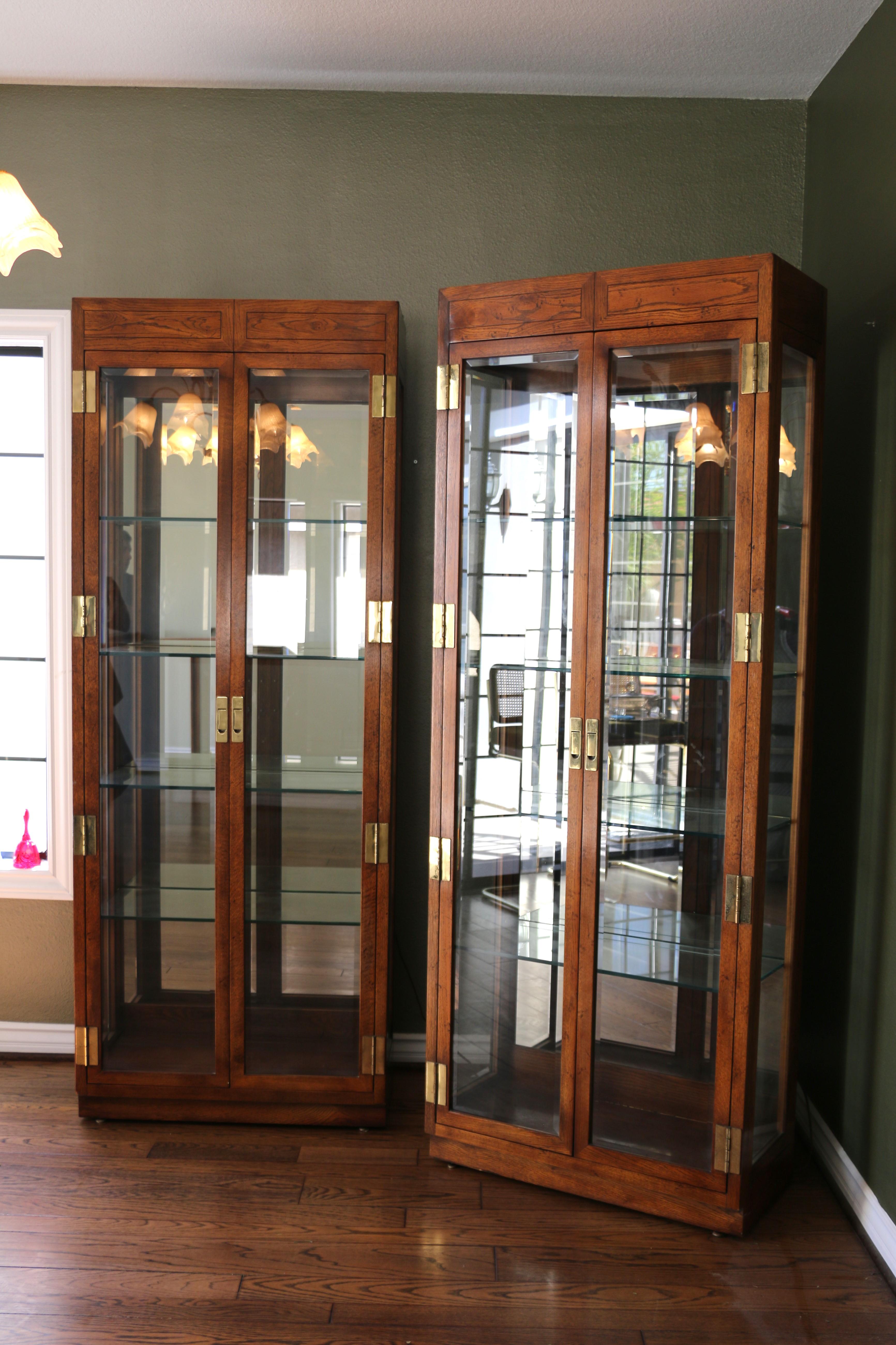Wonderful  pair of 1980’s Campaign Style Curio Display Cabinets designed by Henredon. They have the label in the back, shown in the pictures. Additionally, they are made of wood, brass and glass. Both of them have four adjustable glass shelves with