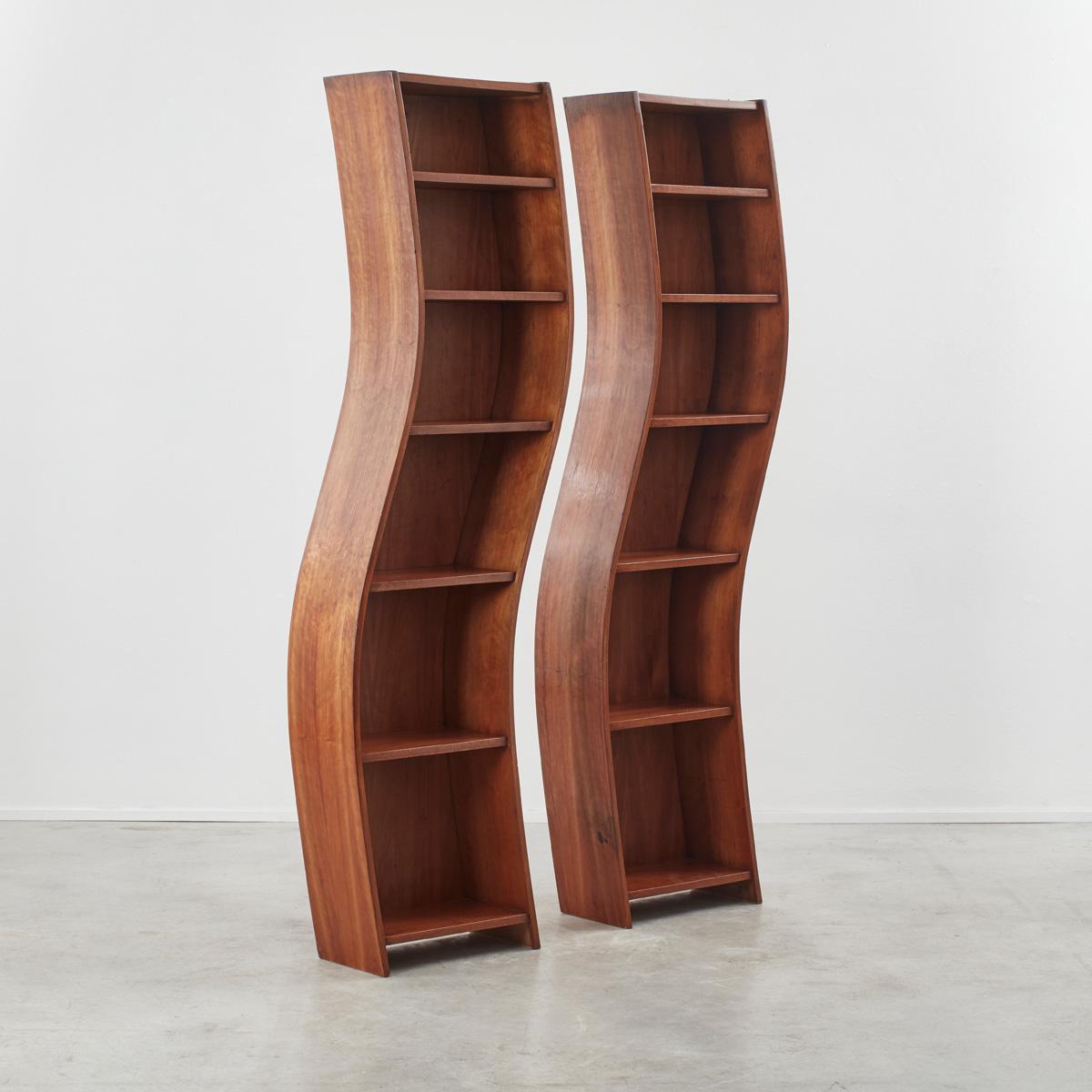 A duo of wavy wooden bookcases. Very beautiful tone to the wood and pleasing synchronistic forms. 

Some restored water damage to the tops, but still functional and easy on the eye. The wood is relatively light – we would recommend fixing to the