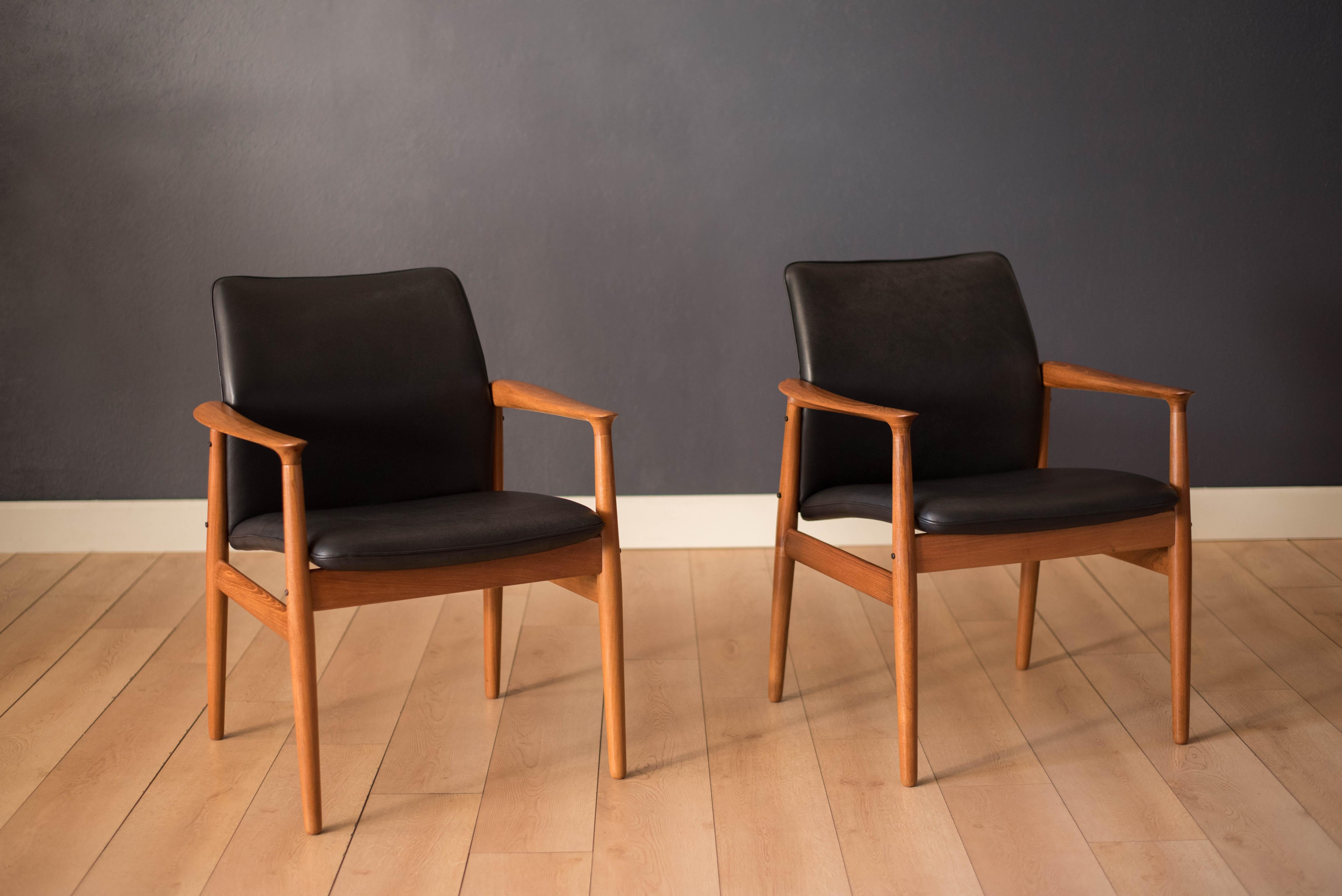 Mid-Century Modern pair of lounge armchairs designed by Grete Jalk for Glostrup Møbelfabrik. This set features sculpted teak arms and a comfortable curved backrest. They have been professionally reupholstered in black leather with brand new foam.