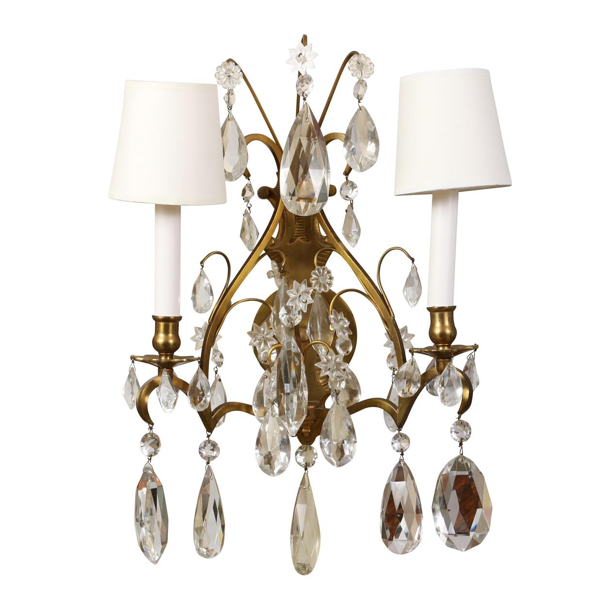 A vintage pair of two arm sconces with arched gilt metal back and large hanging crystals from multiple tiers for a beautiful effect with both heavy crystals and smaller rosettes.