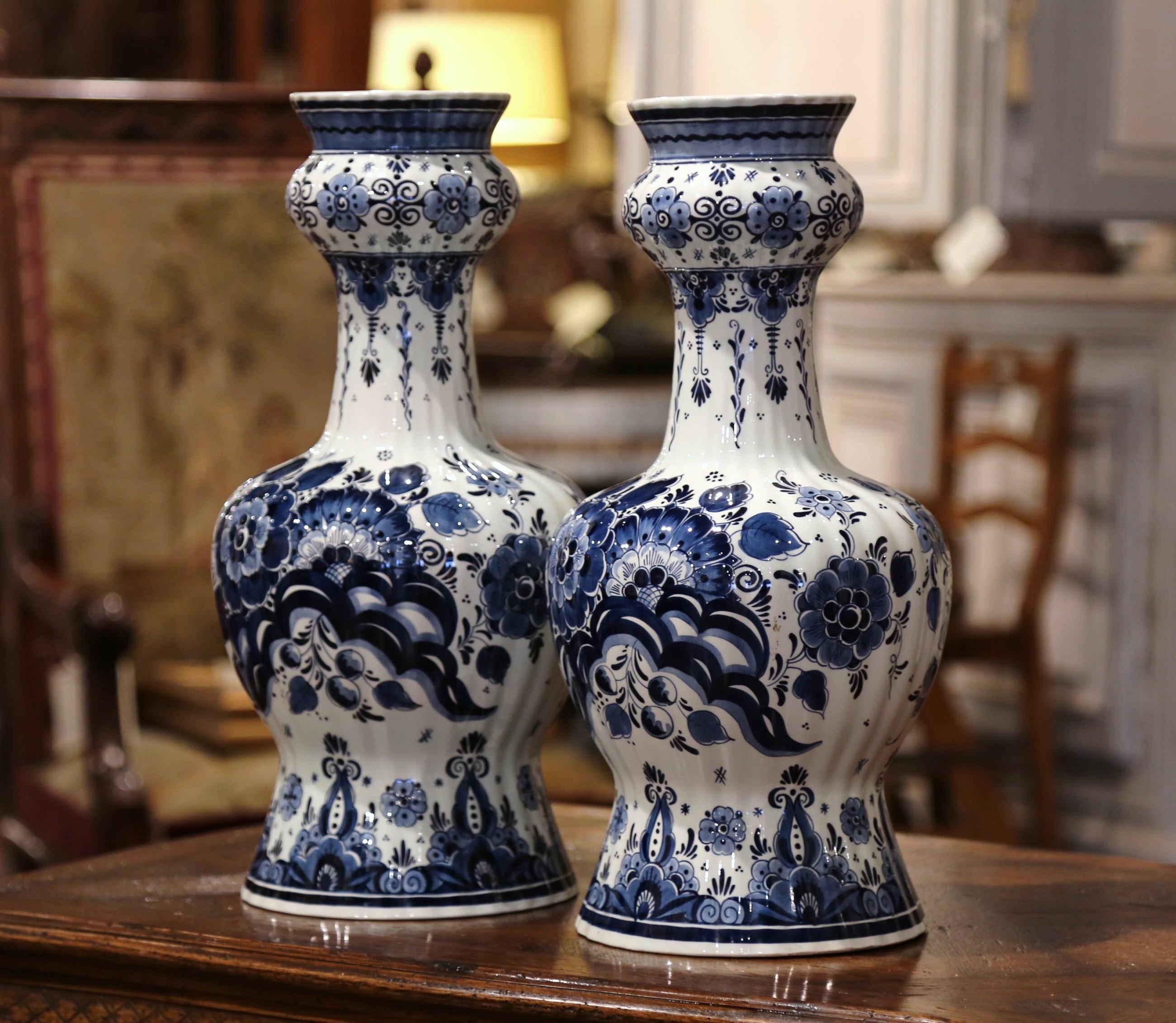 Created in Holland, circa 1980, these tall ceramic delft vases are round in shape with a long swollen neck; the double Gord flower vases feature traditional hand painted floral and leaf decorations in a Classic navy blue and white palette. Both