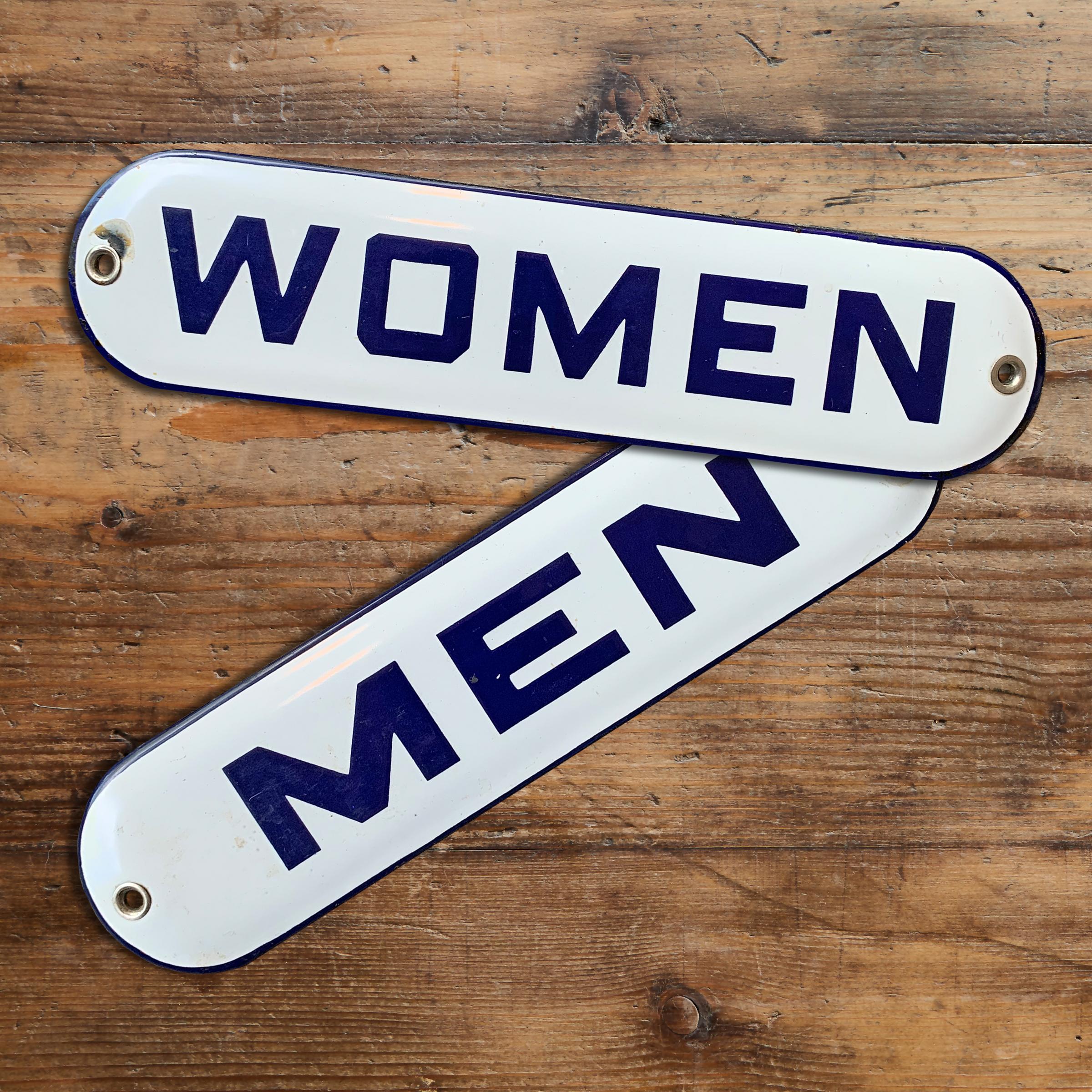 A pair of vintage American porcelain enameled iron restroom signs with large blue block letters against white backgrounds.