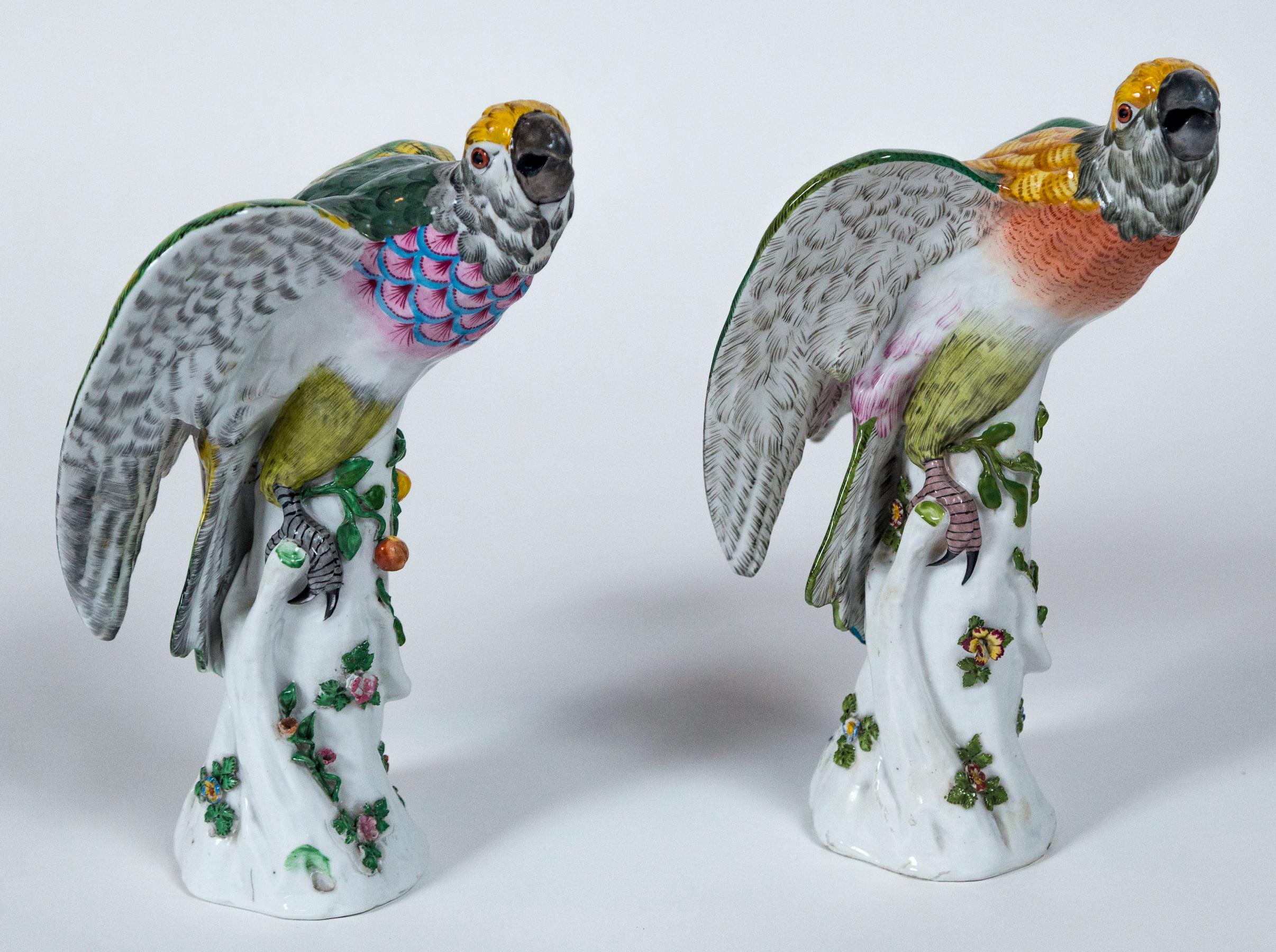 Pair of vintage European porcelain parrots. Beautifully detailed with colorful glazing. Parrots are perched on tree trunks with appliquéd floral designs.