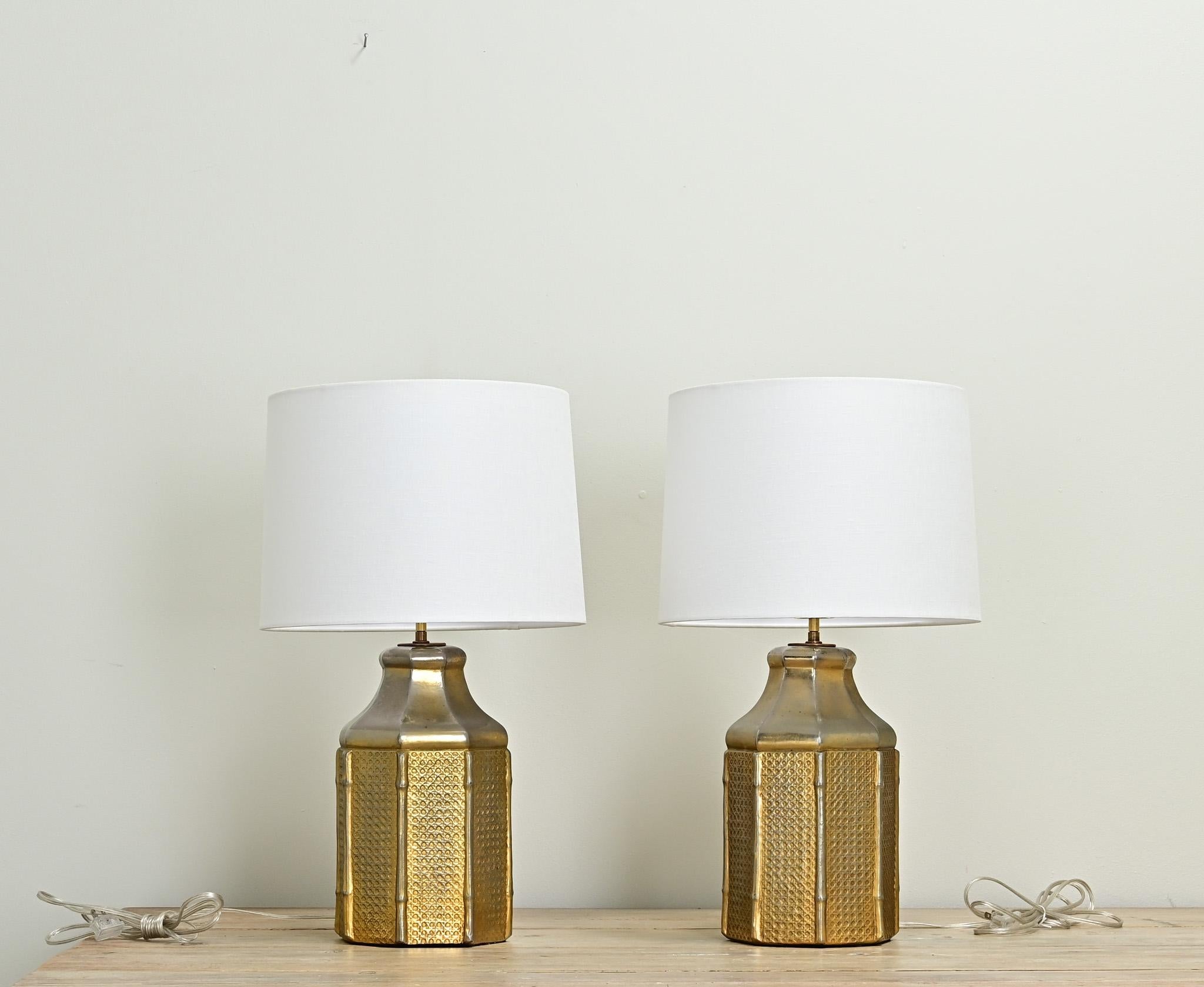 A vintage pair of faux cane and bamboo lamps made of metal. Each lamp is hexagonal in shape with faux bamboo supports between woven faux cane. New linen drum shades compliment the lamp bases well. This pair of lamps have recently been professionally