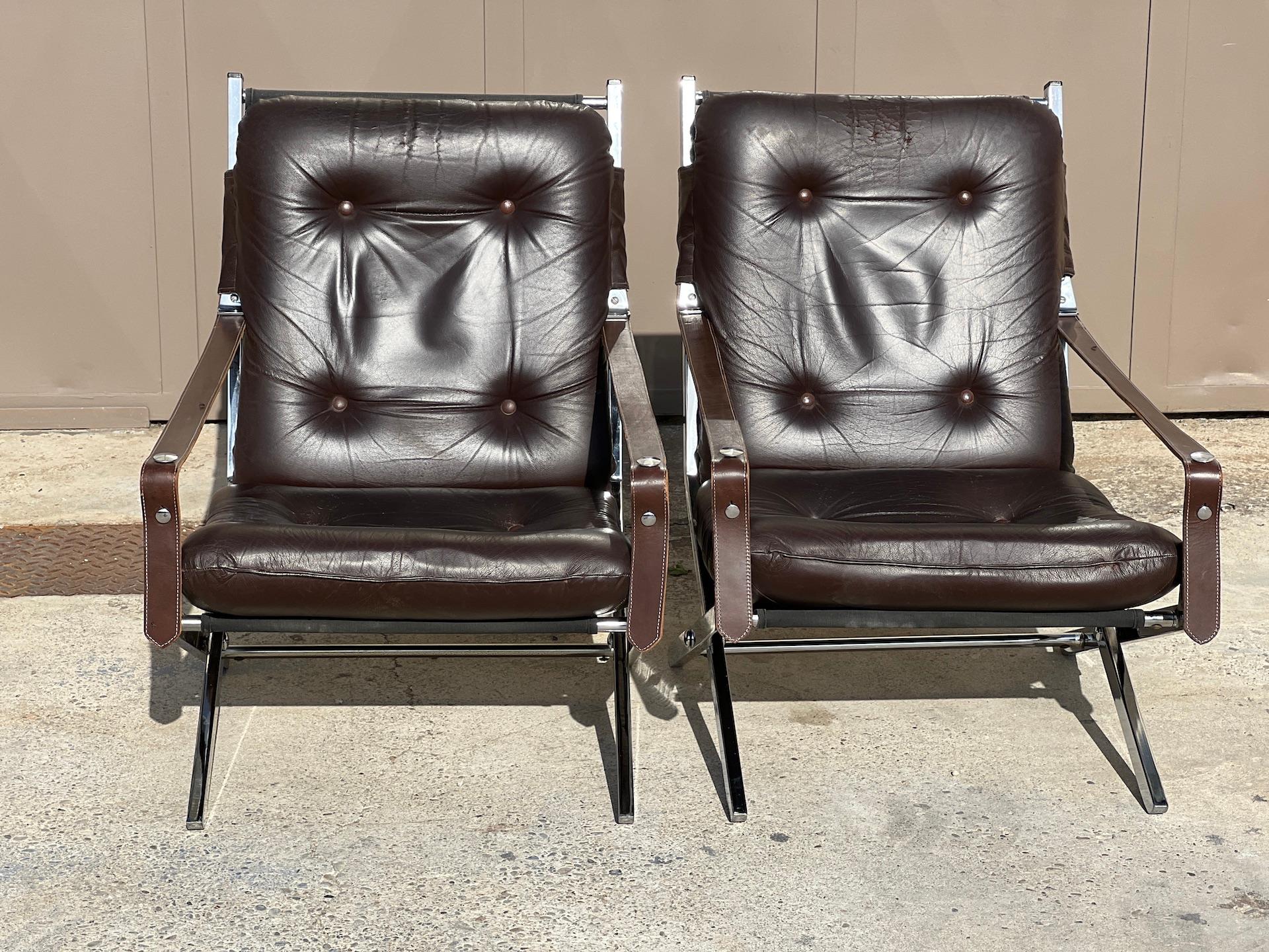 Pair of folding armchairs by Robert Duran 1970. Structure is in chromed metal. The seat and back in chocolate leather. Armrests with adjustable leather straps. In good condition, the leather has a nice patina.