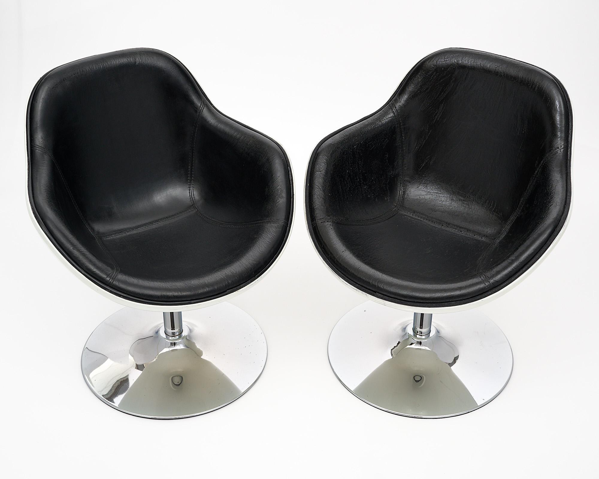 Pair of armchairs in the French modernist style. The vintage armchairs feature an ivory polyurethane shell with an original black vinyl upholstery inside. The armchairs swivel on a chromed steel center foot.