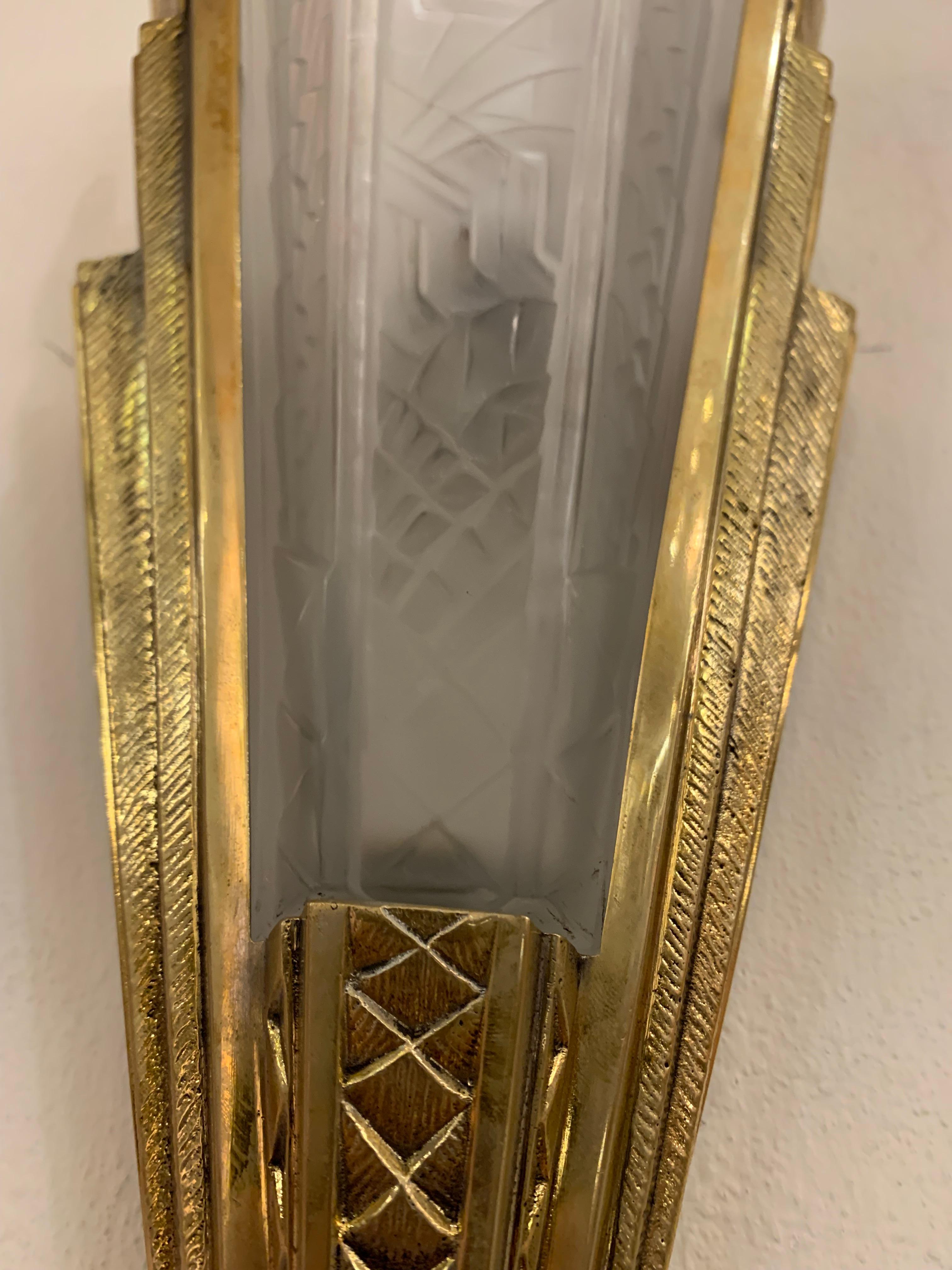 Gorgeous pair of vintage Art Deco sconces signed by Pierre Maynadier. They are in patinated brass and glass that was pressed and molded, typical of the mid-century creations. Both hardware and glass wear geometrical designs, also typical of the