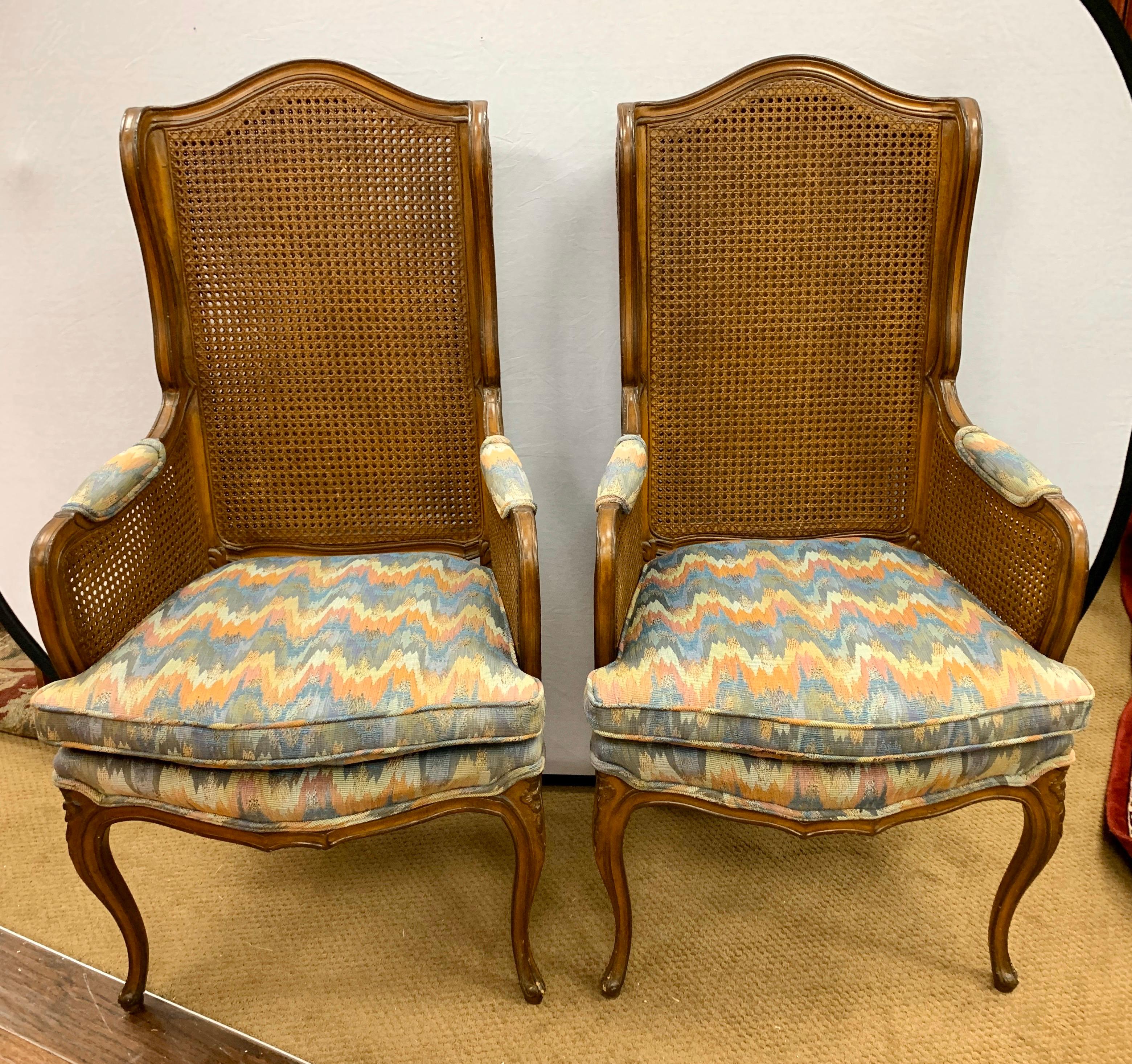 French caned back wingbacks feature an airy cane backing on arms and back and have an exposed trim with carved details. They are upholstered in original chevron print fabric on the seats and padded arm.