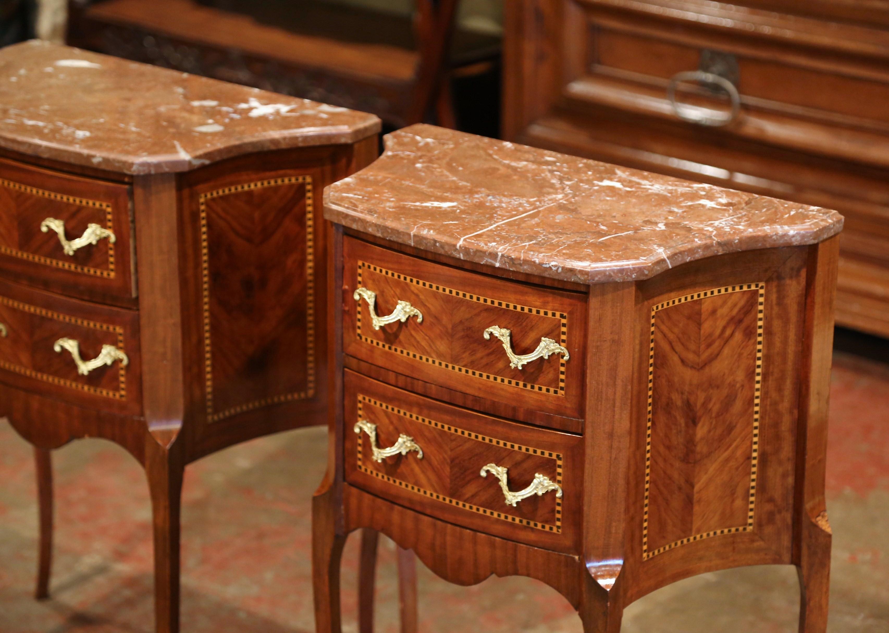 Crafted in France, circa 1920, the antique nightstands sit on cabriole leg embellished with front bronze caps over the feet. Each cabinet has curved sides, and two drawers across the front decorated with inlay marquetry work and bronze handles over