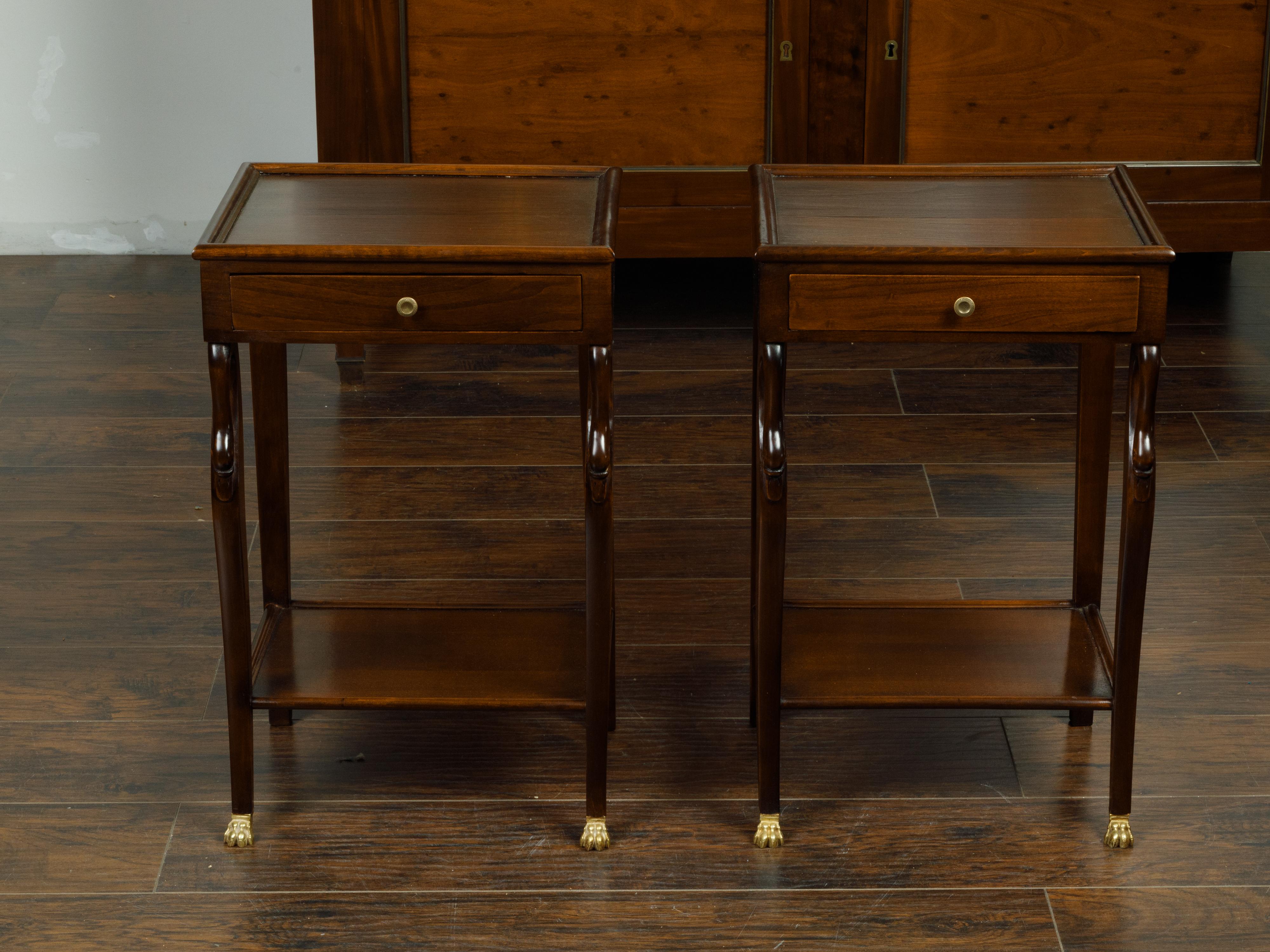 A pair of French Empire style mahogany bedside tables from the mid 20th century, with swan motifs and brass paws. Created in France during the midcentury period, each of this pair of mahogany tables features a rectangular top with inset board,