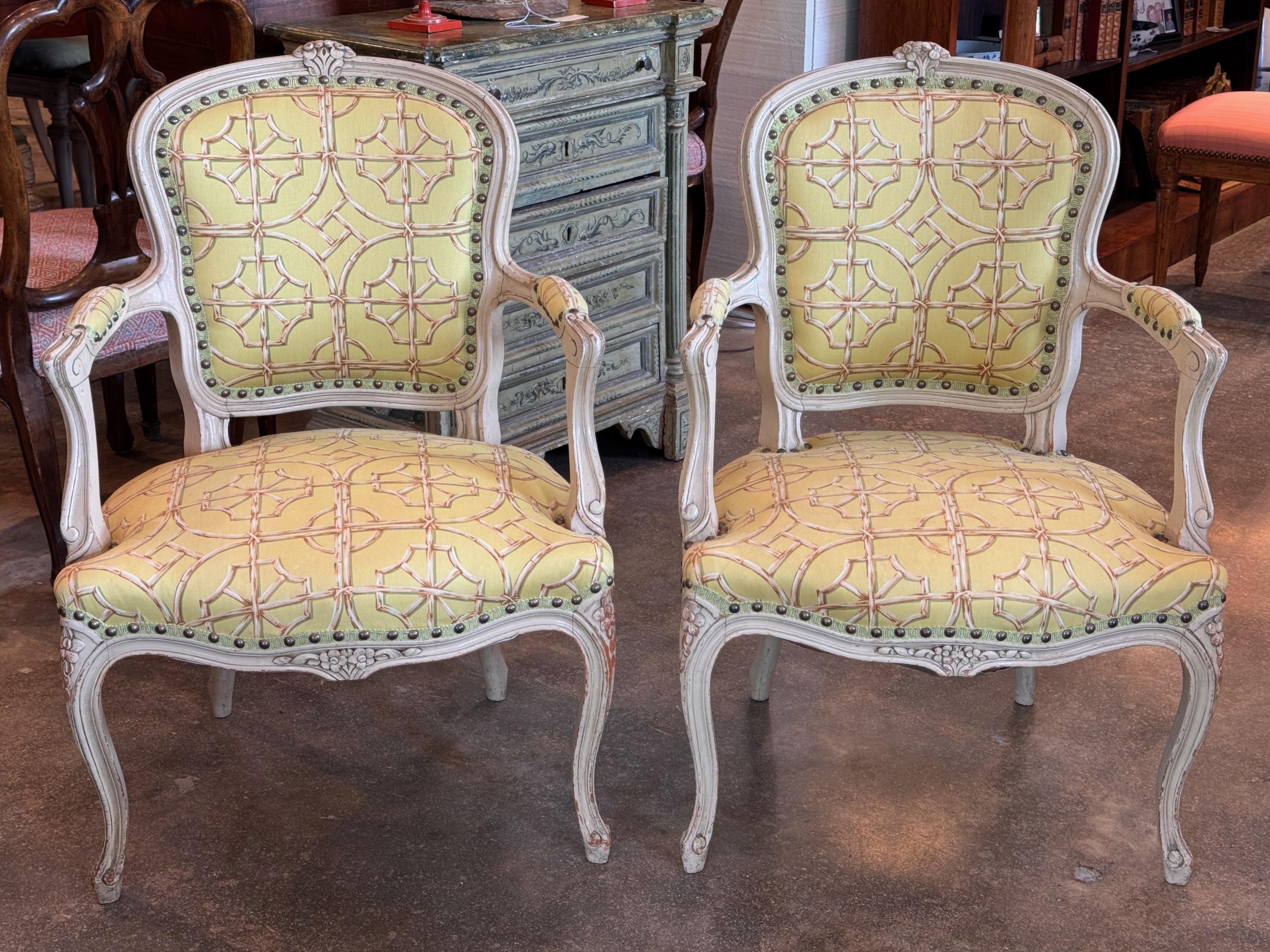 Paire de fauteuils français vintage avec des cadres en bois sculpté et des dossiers en forme. Finition peinte avec une légère détresse et rembourré dans un tissu jaune à motifs avec une garniture de tête de clou. Les accoudoirs incurvés et les pieds