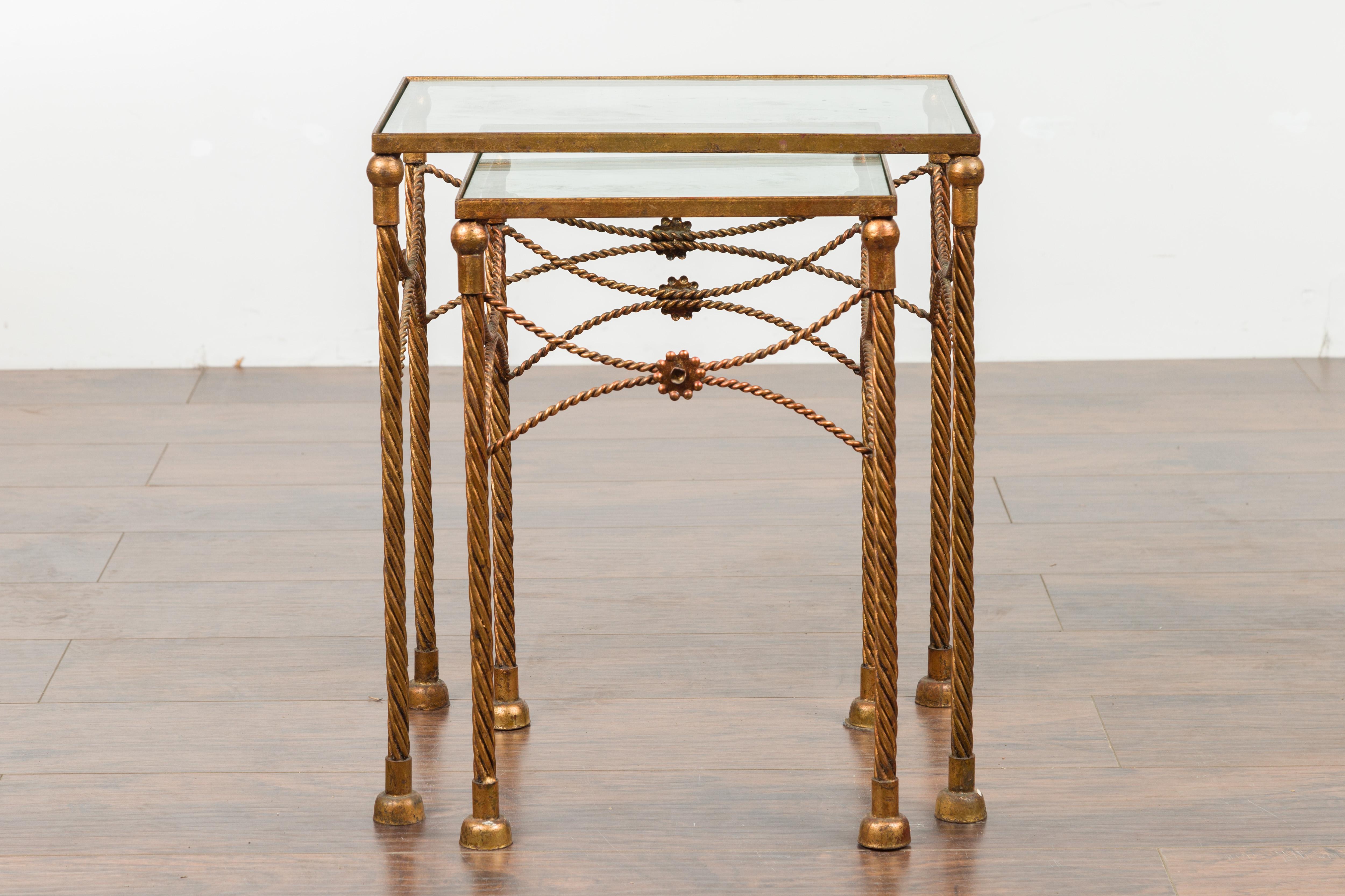 A pair of vintage French gilt metal nesting tables from the mid-20th century, with glass tops, twisted design and floral motifs. Created in France during the midcentury period, each of this pair of 