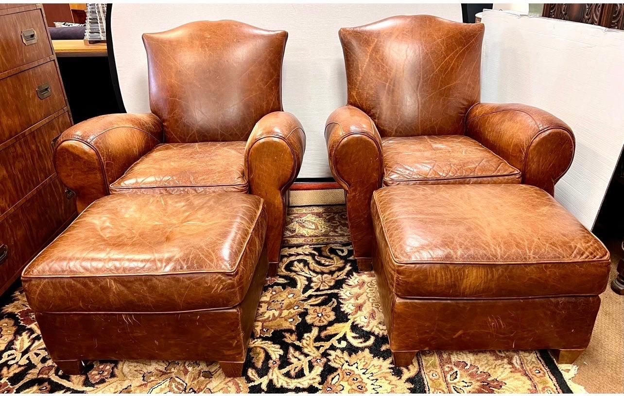 Elegant pair of vintage French mustache back club chairs, with matching ottomans, that have been aged to perfection with coveted distressed patina only acquired through age and use. The leather is a luxurious caramel brown. The chairs are oversized