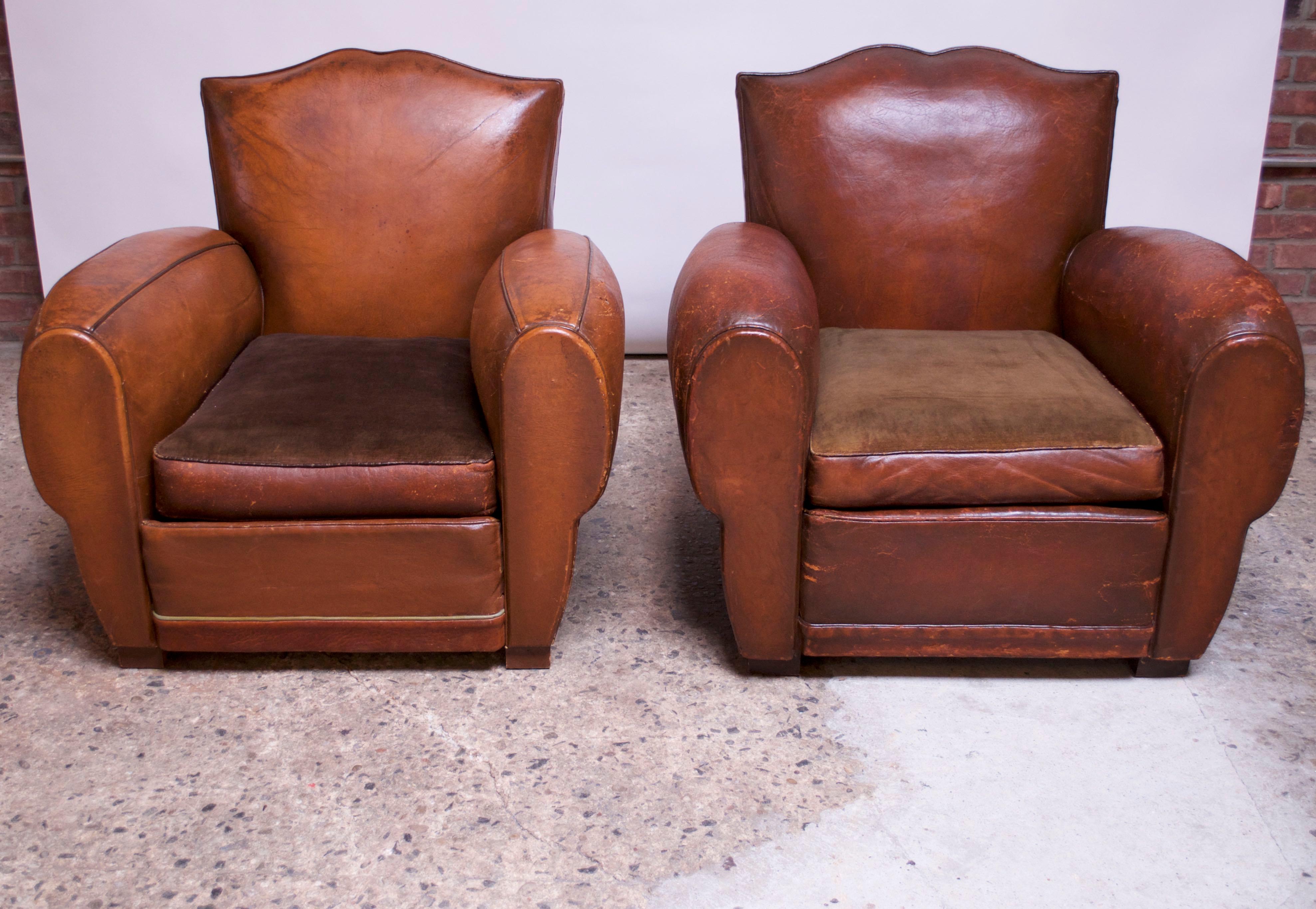 Circa 1930s French club chairs with 'mustache' backs, originally sold as 'his and hers,' given the slight aesthetic and proportional differences (the chair with the seamed arms is slightly smaller, the leather differs in color, and the stud or