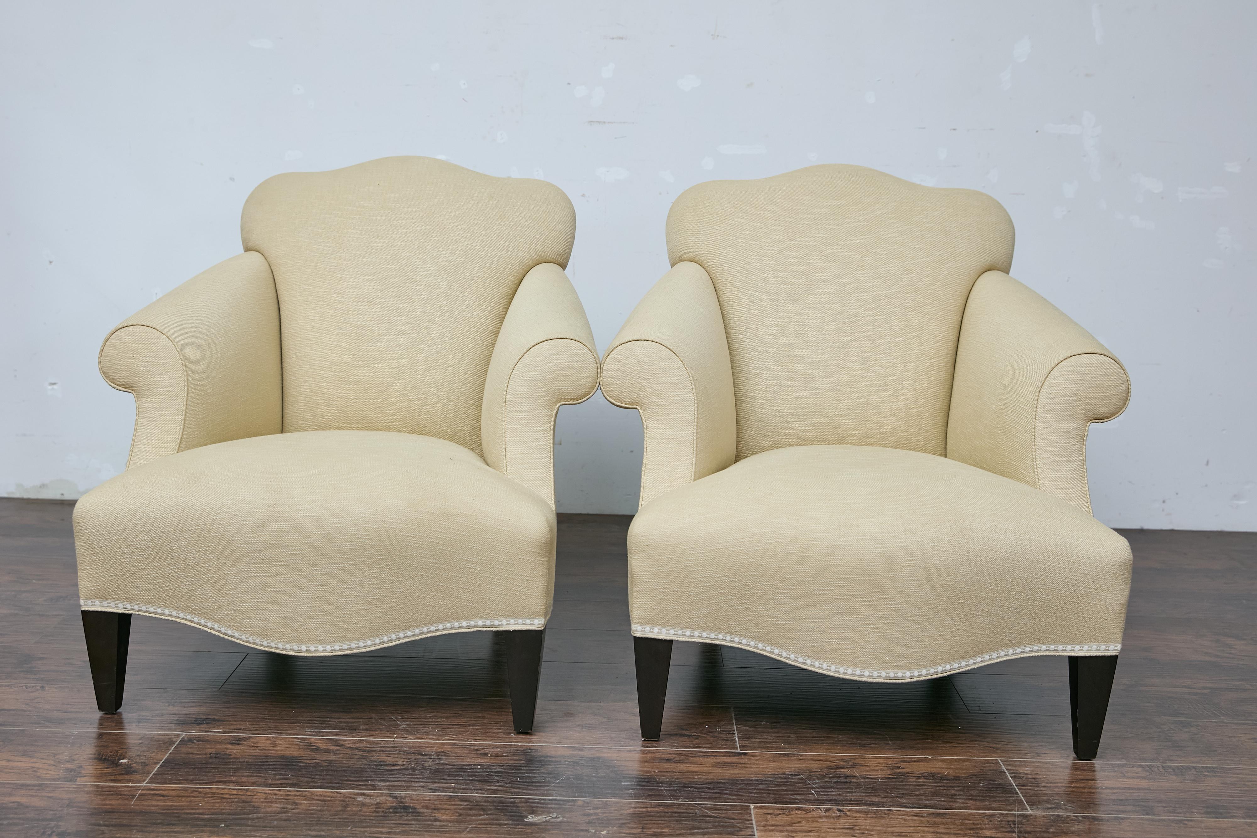 A vintage pair of French lounge chairs with rolled arms, camelbacks, ebonized legs and upholstery. This vintage pair of French lounge chairs, with their elegant camelbacks and rolled arms, exudes classic sophistication and comfort. The chairs rest