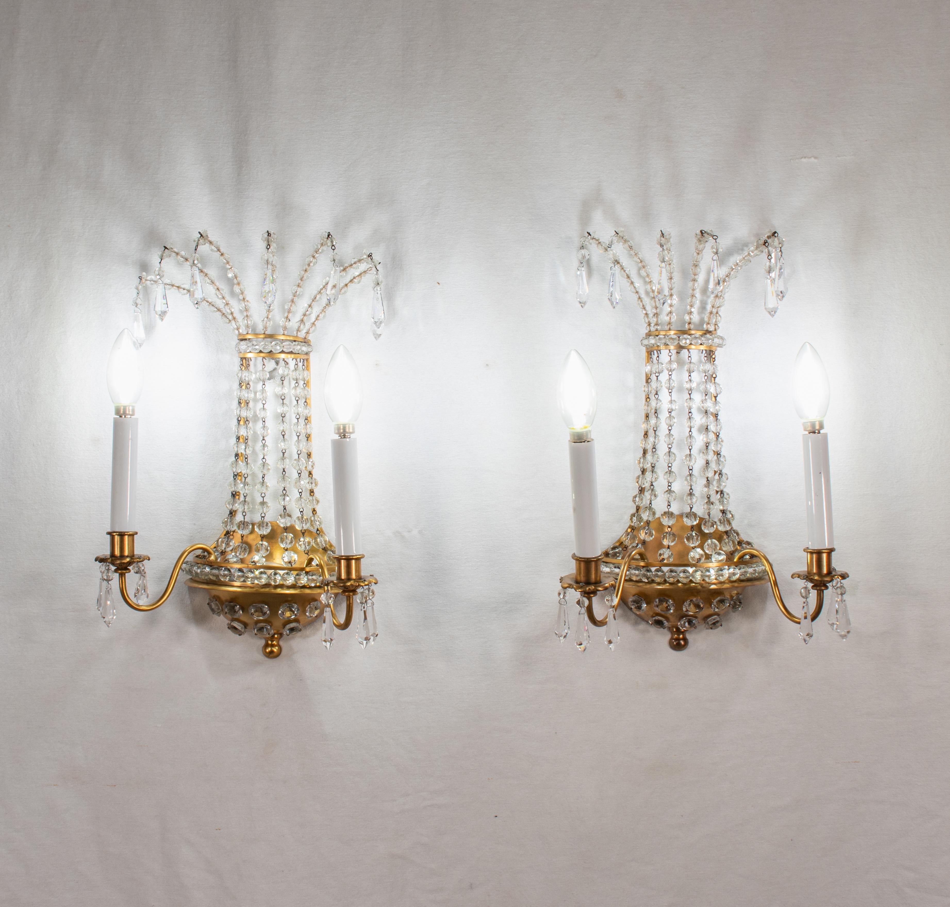 These Empire-style sconces showcase a signature element of Maison Jansen lighting: pierced brass encrusted with beaded crystals. This intricate combination of brass and encrusted crystal beads creates a stunning visual effect resembling a