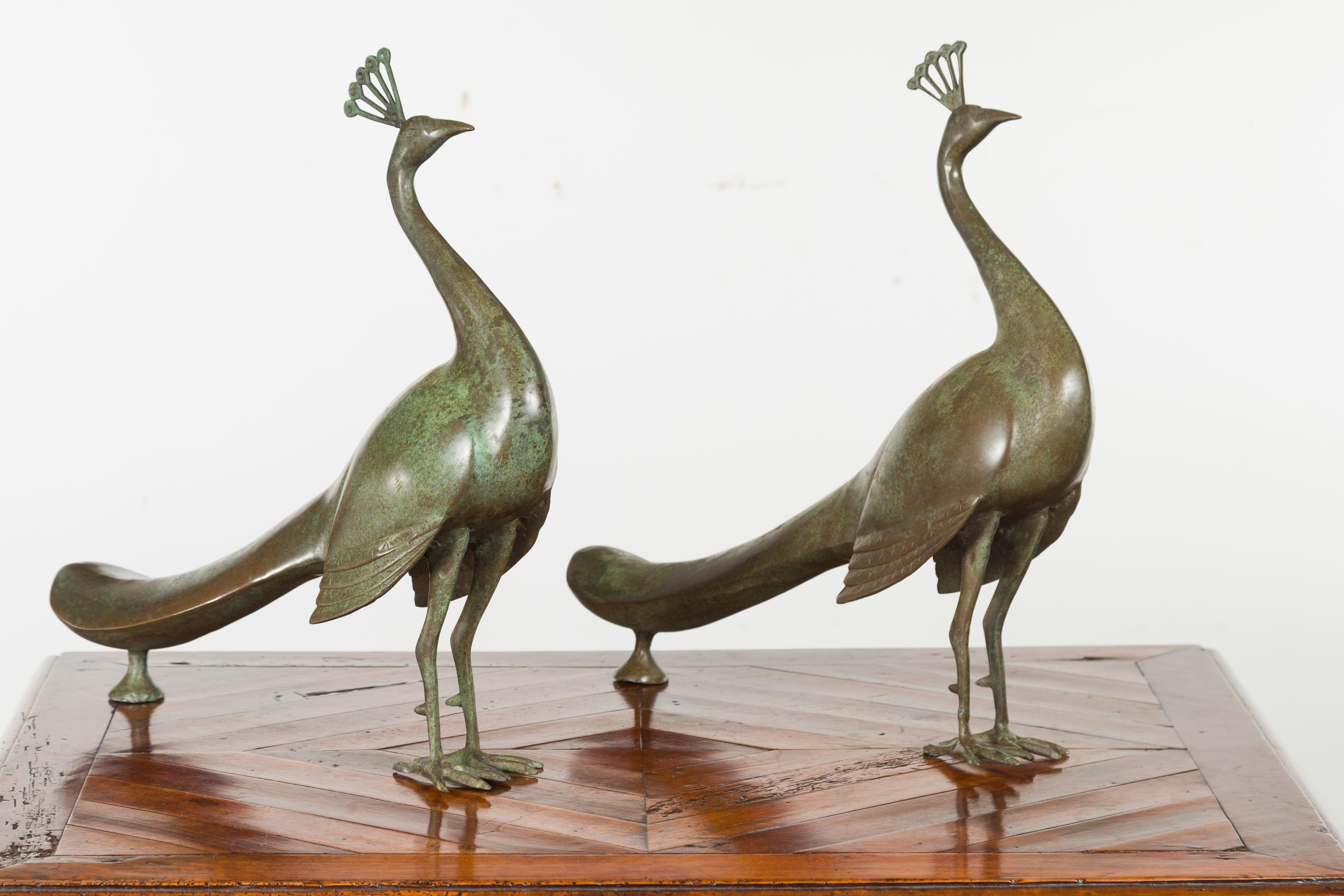 A pair of French metal peacocks from the mid-20th century, with verdigris patina. Created in France during the midcentury period, each of this pair of metal sculptures depicts an elegant peacock standing proudly on its two legs. Topped with a corona