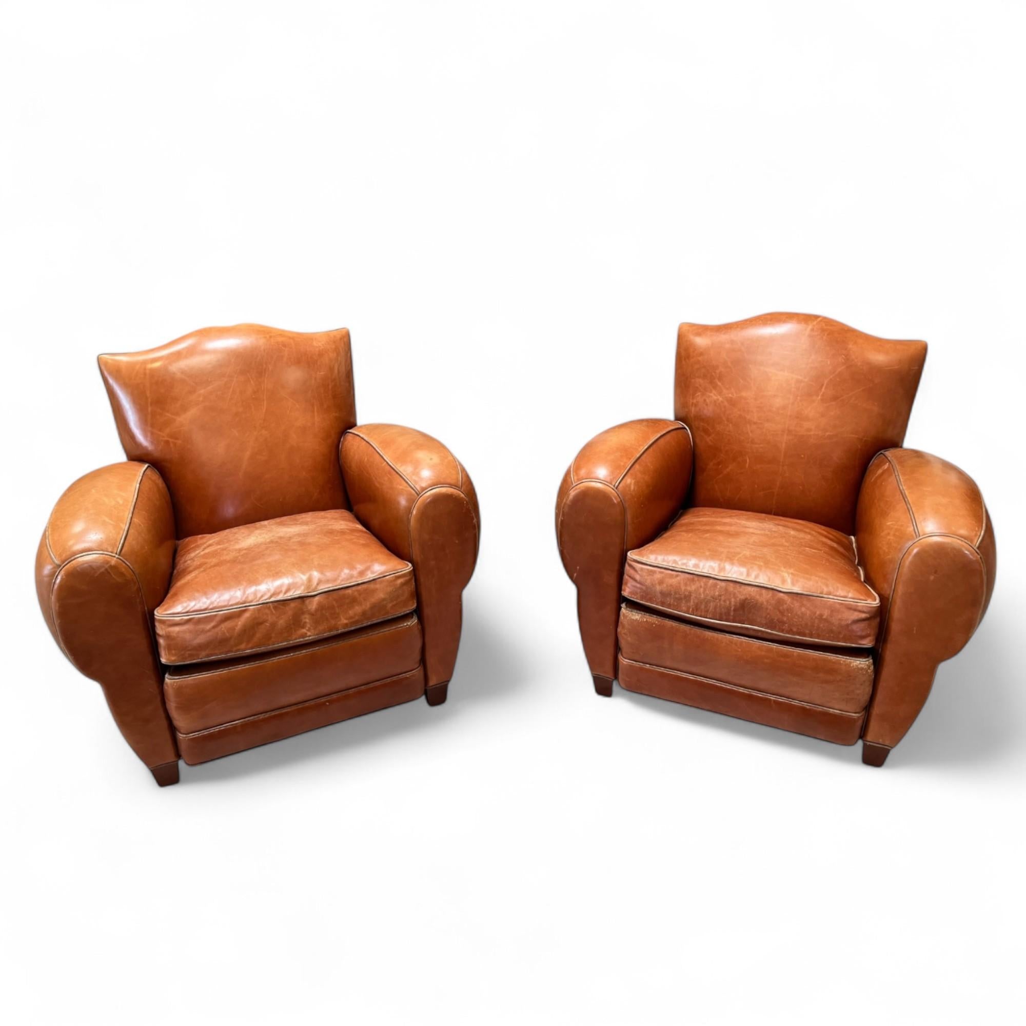 Questa coppia di sedie a baffi in pelle vintage conferisce uno stile da club francese senza tempo, grazie alla ricca patina e ai caratteristici schienali smerlati. Realizzate in pelle color caramello invecchiata, offrono carattere e comfort grazie