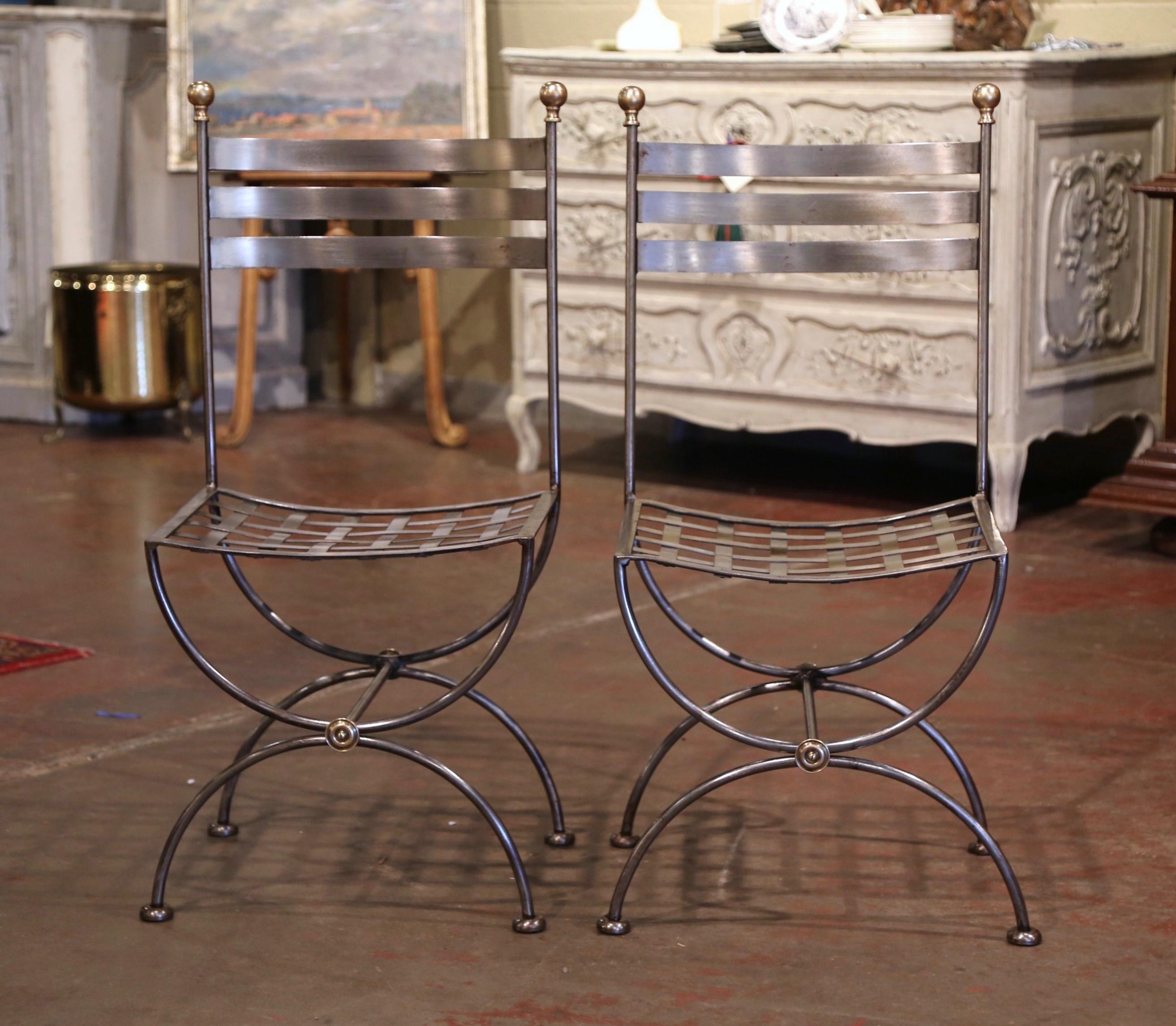 Place these two vintage chairs around a bistrot table, or outside on a patio! Crafted in France circa 1980 and made of wrought iron, each chair stands on forged Dagobert (or Curule) legs and features three curved ladders on the back, embellished