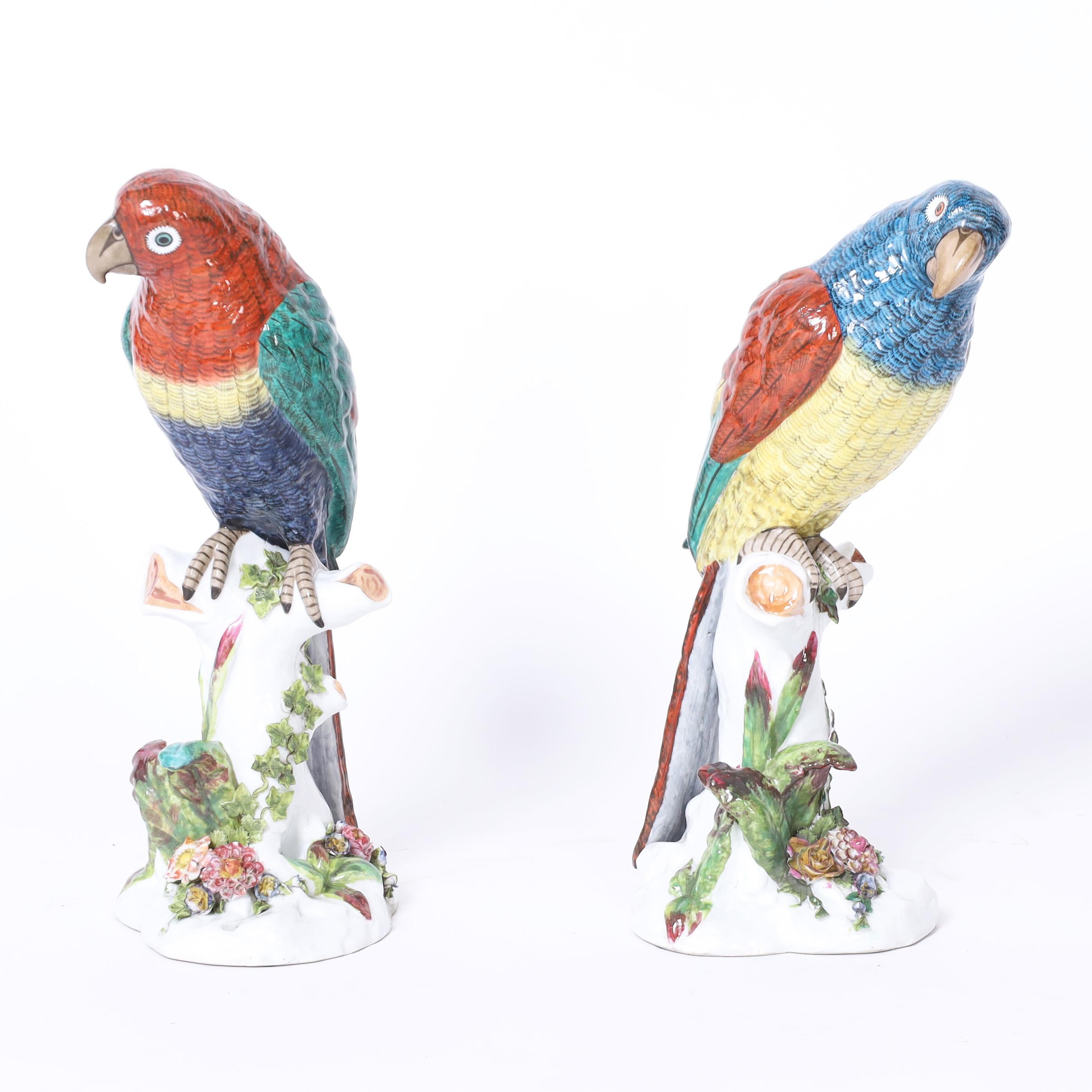 Standout pair of life size French porcelain parrots perched on tree trunks, hand decorated in striking tropical colors. Signed by the maker on the bottoms.
